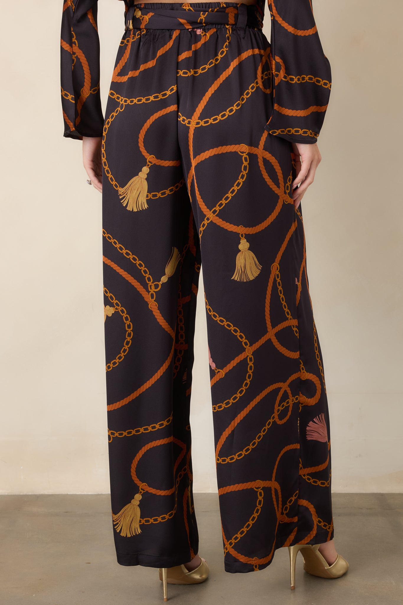 Rear view of the black satin-feel pants showcasing the relaxed wide-leg silhouette and allover ornate print.