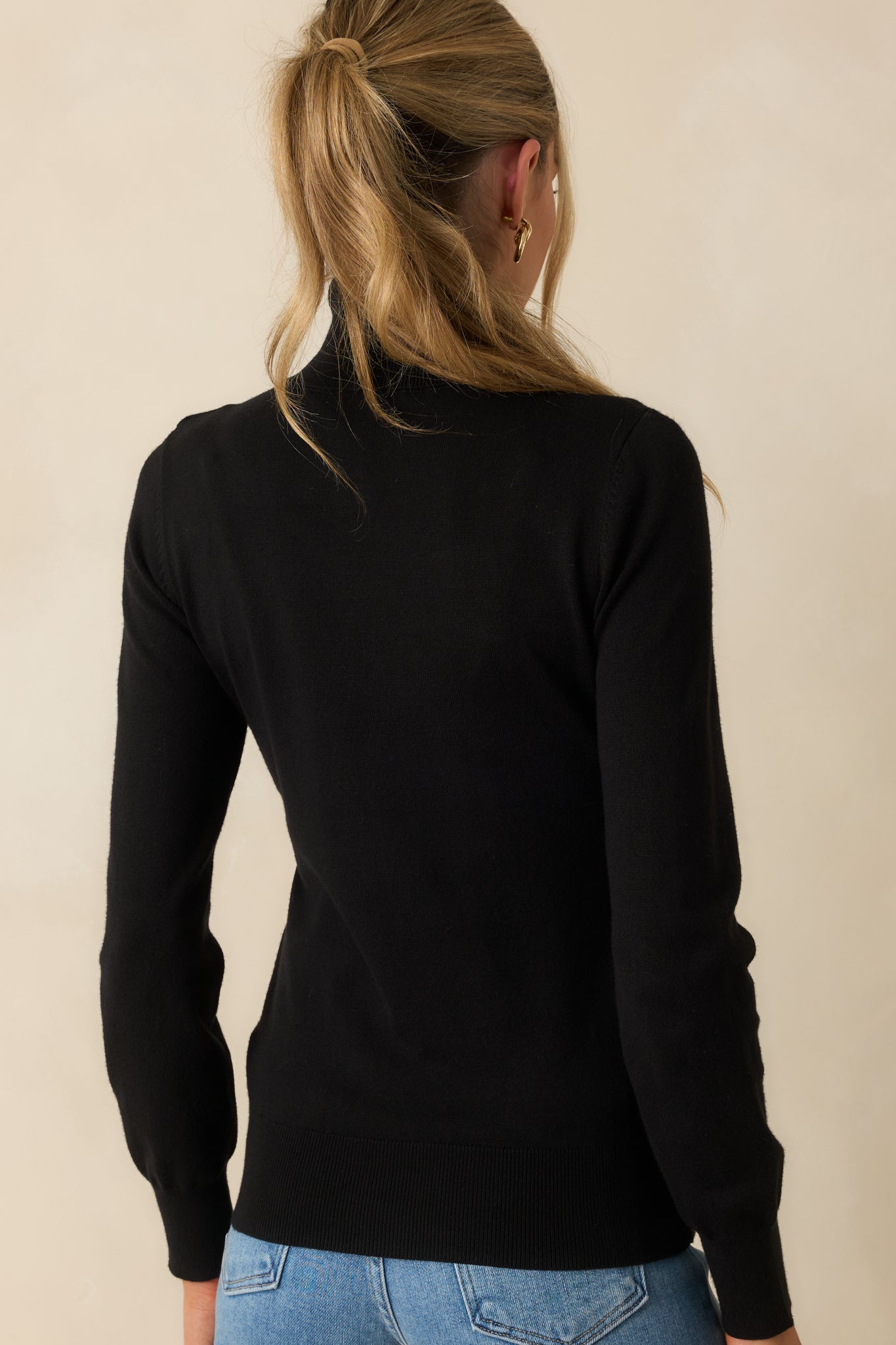 Rear view of the black turtleneck sweater featuring smooth knit fabric and a gently tapered ribbed hem.