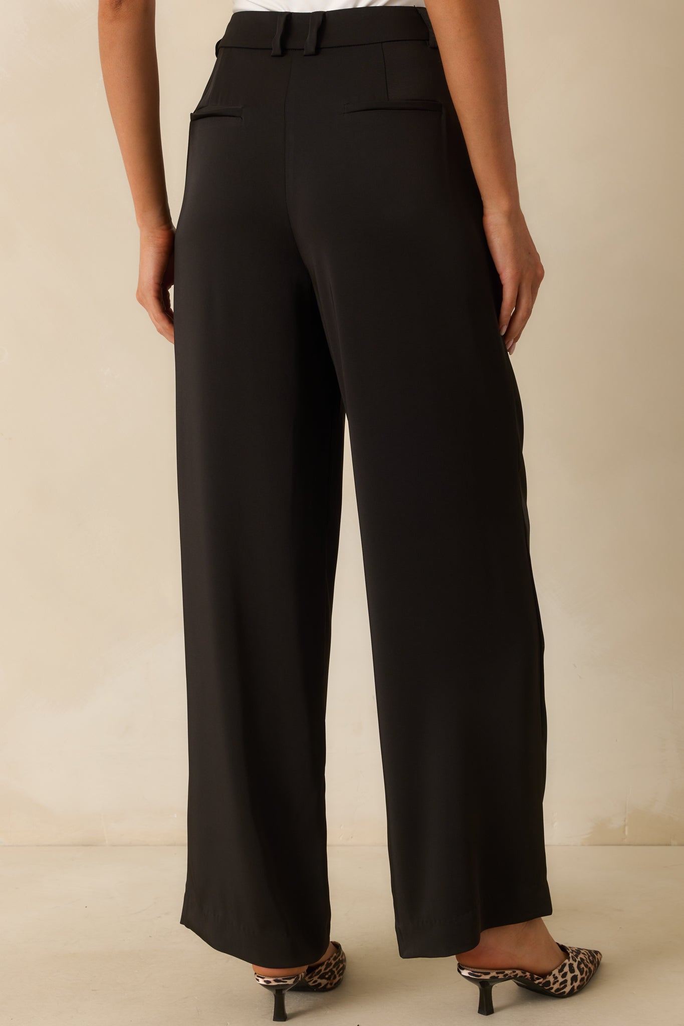 Rear view of black wide-leg trousers, featuring faux back welt pockets and smooth silhouette.