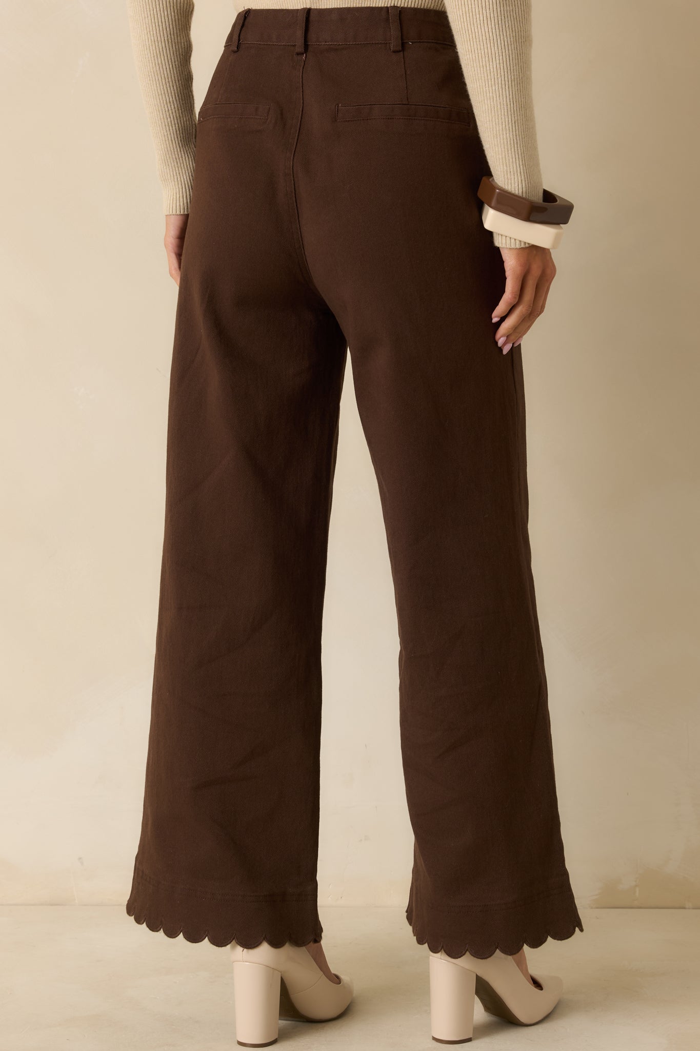 Rear view of brown wide-leg pants showing back welt pockets, belt loops, and scalloped hemline.
