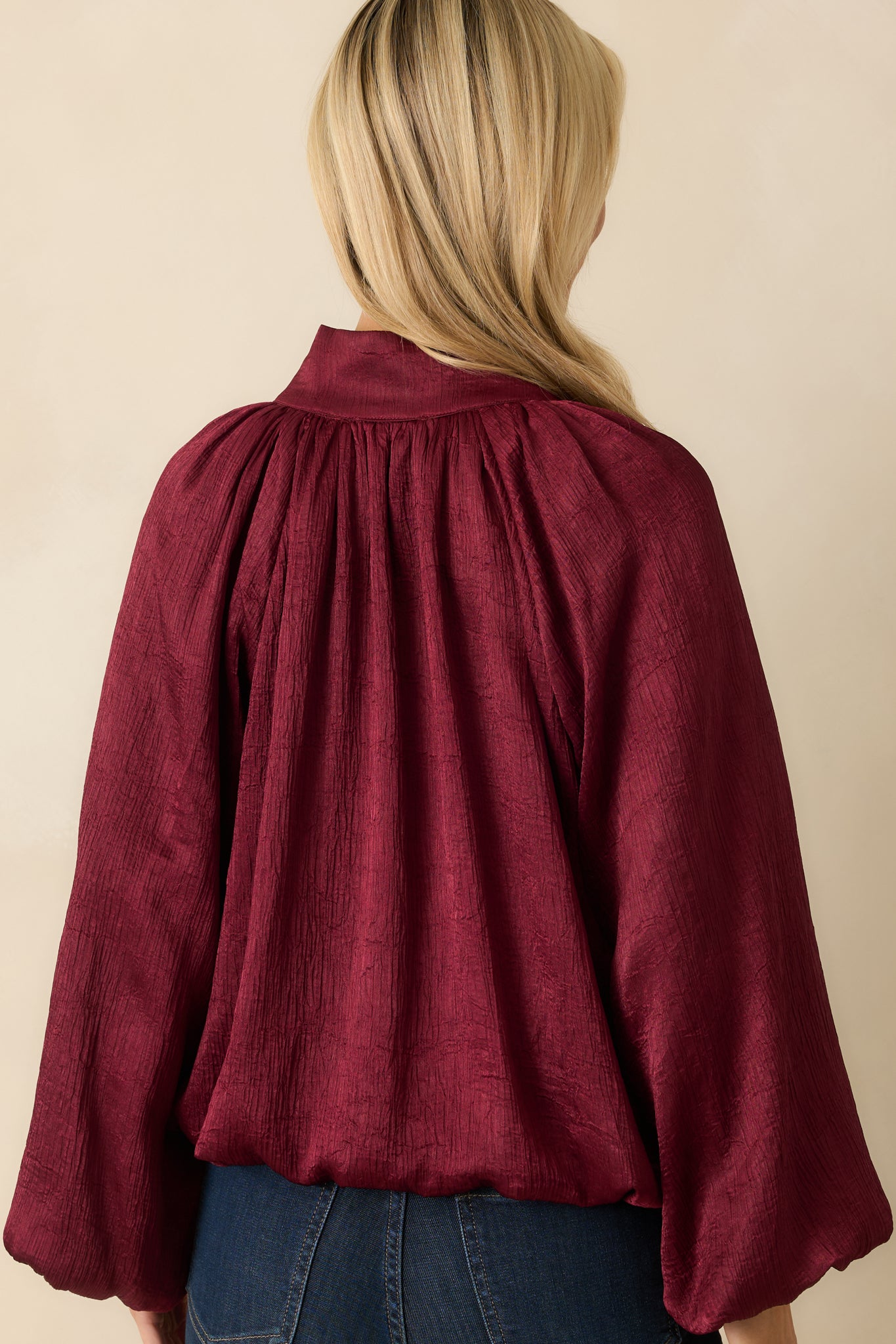 Rear view of the burgundy satin V-neck top highlighting the relaxed silhouette and long peasant sleeves.