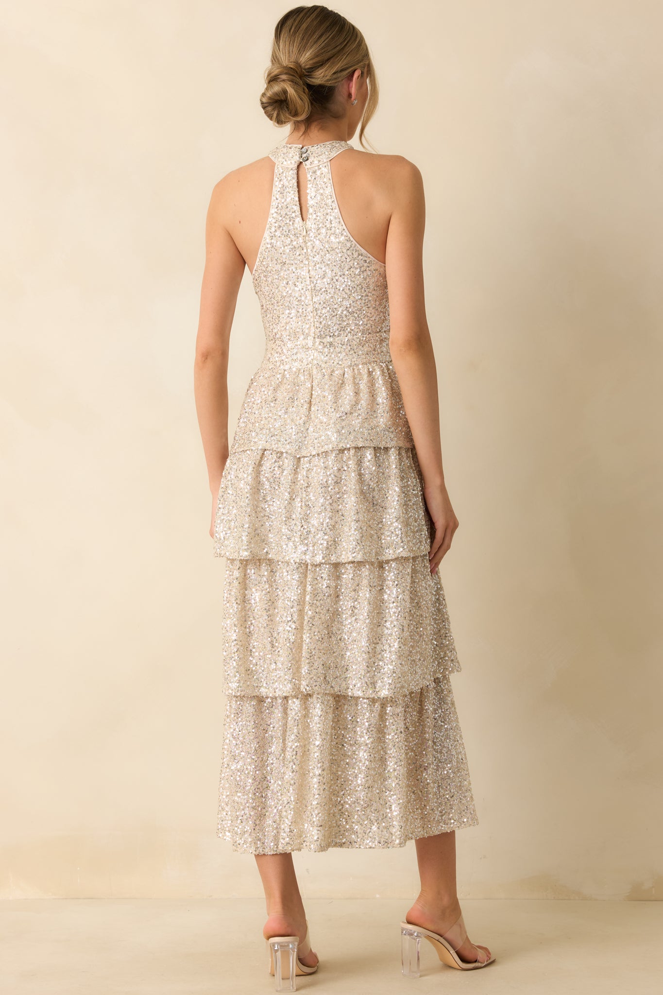 Rear view of the champagne sequin maxi dress showing the halter neckline, back zipper, and tiered skirt flow