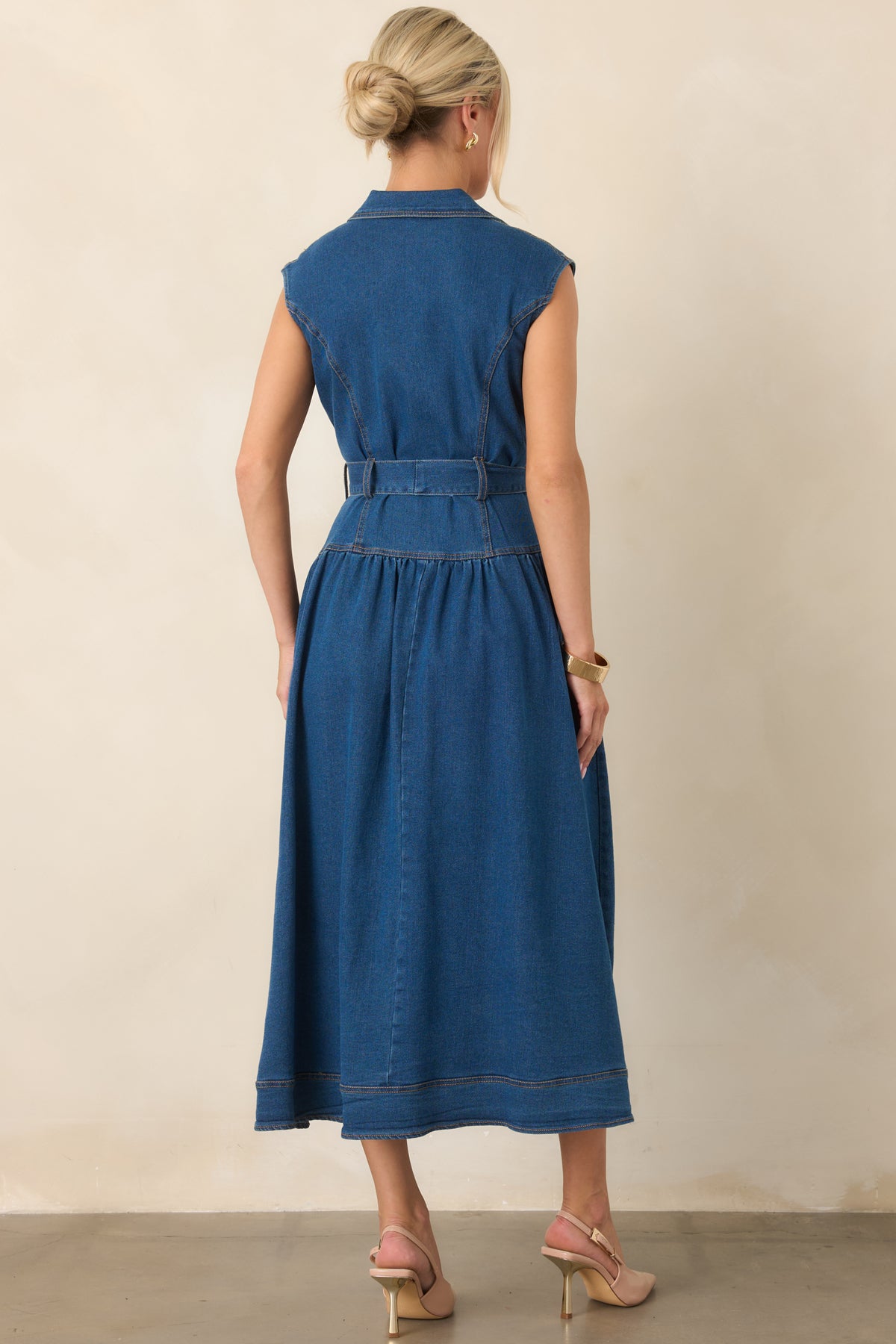 Rear view of the dark wash denim midi dress showcasing its sleeveless silhouette, tailored shape, removable waist belt, and clean denim construction.