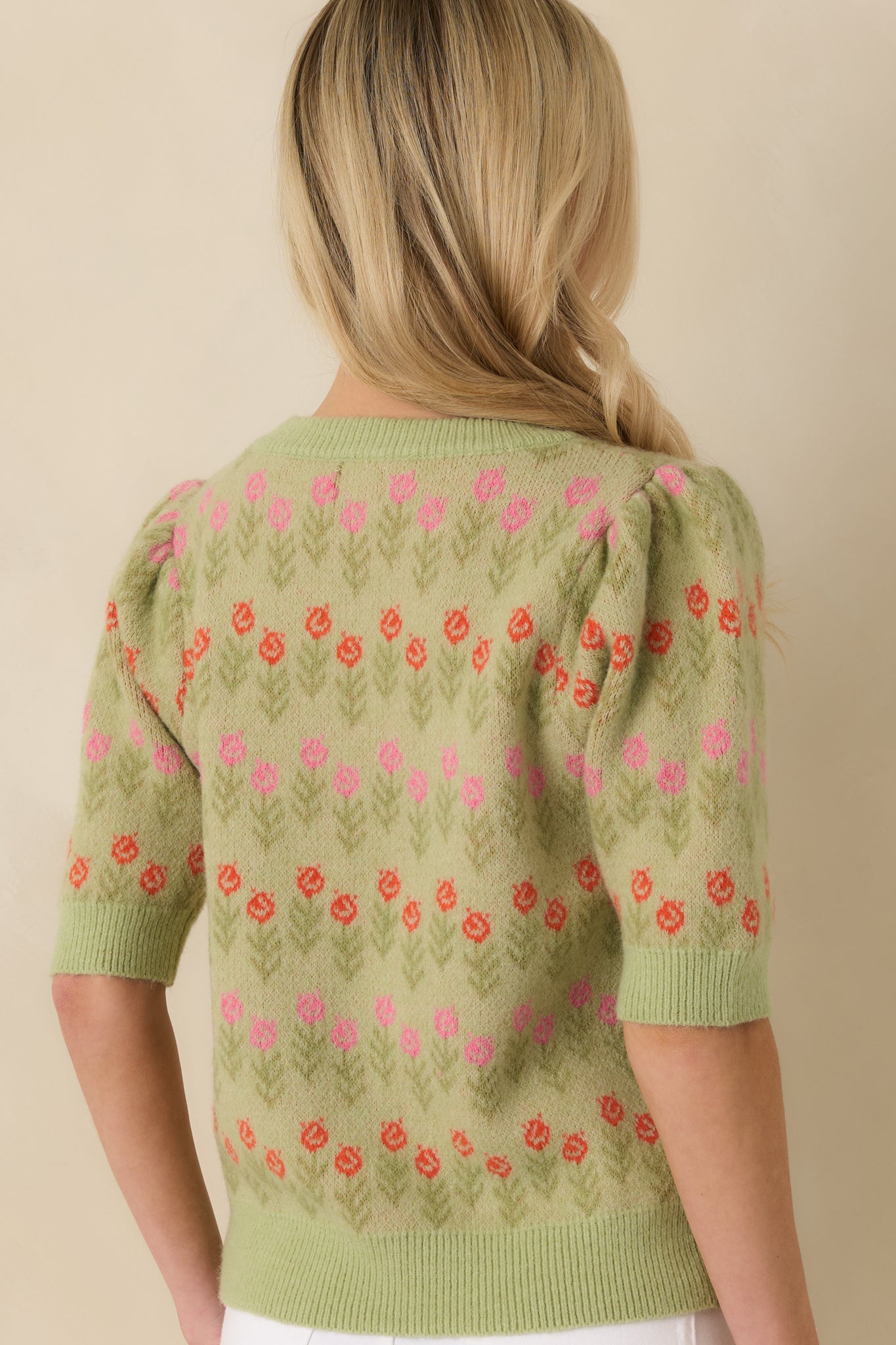 Rear view of light green short sleeve knit sweater displaying floral jacquard and ribbed hem.