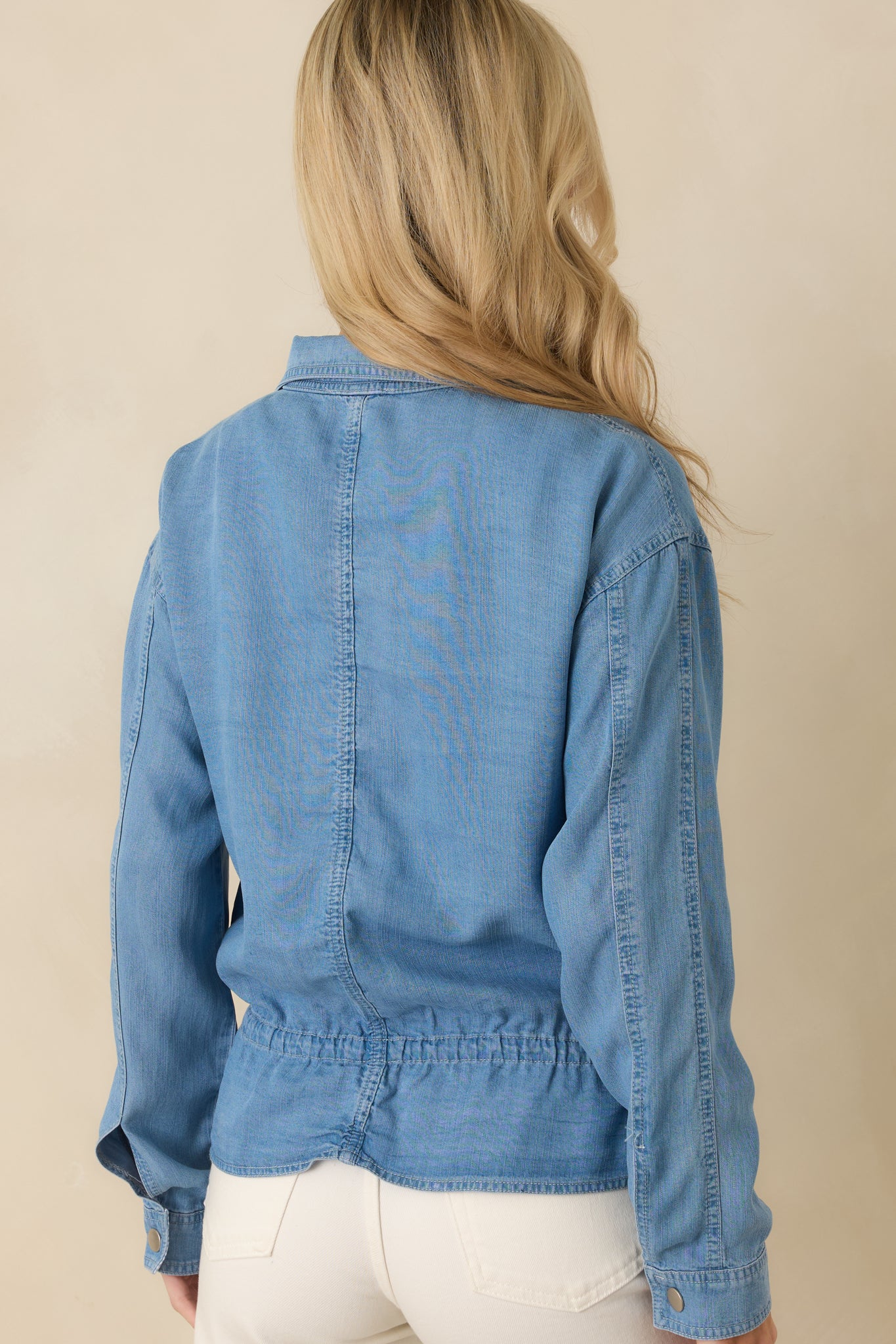 Rear view of the medium wash denim top displaying long sleeves and gently shaped waist.