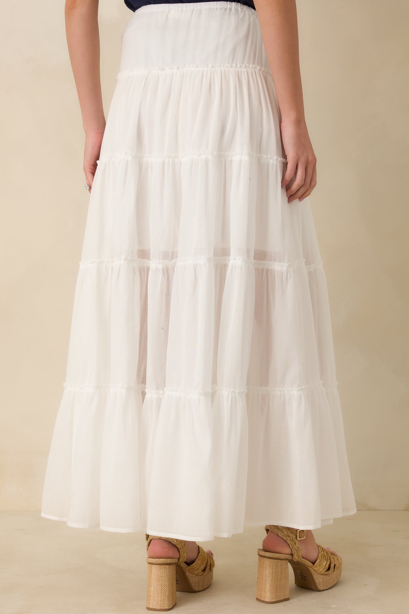 Rear view of ivory maxi skirt featuring elastic waistband with adjustable tie, tiered silhouette, and flowing full-length drape.