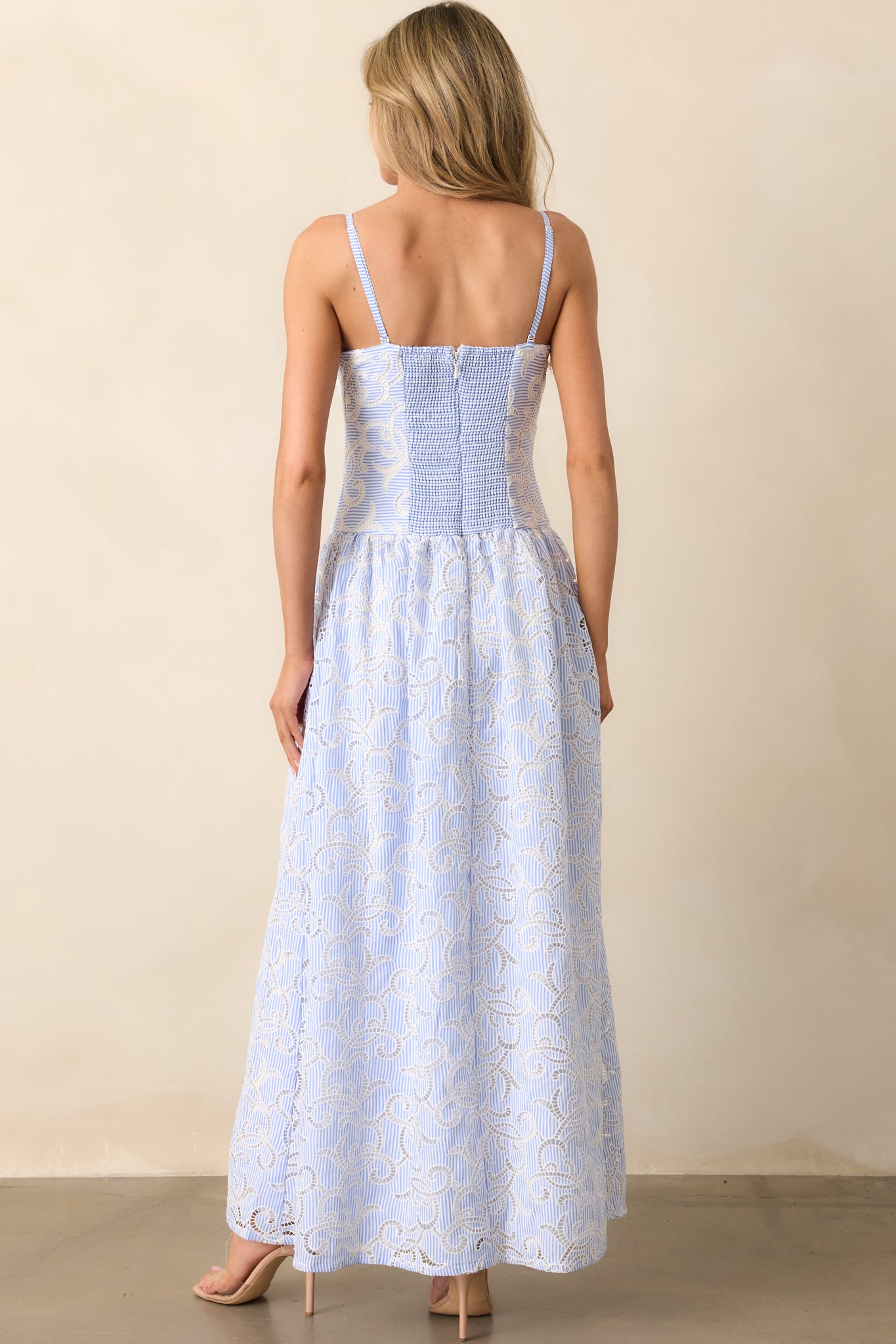 The rear of a blue and white striped maxi dress, featuring a smocked panel for stretch, a hidden zipper, and embroidered eyelet details continuing throughout the design.