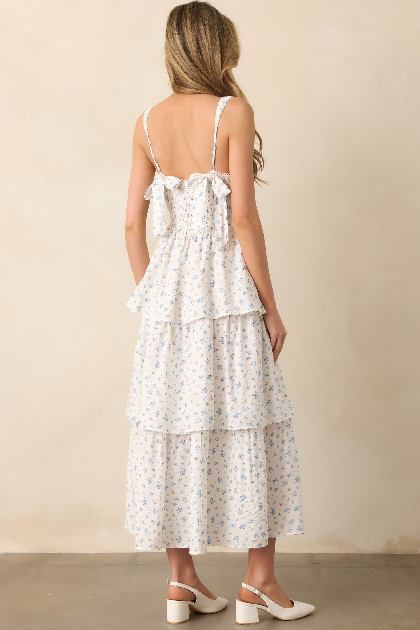 A rear view of the blue floral maxi dress, featuring two back bow details and a smocked back panel. The tiered skirt and adjustable straps complete the design.