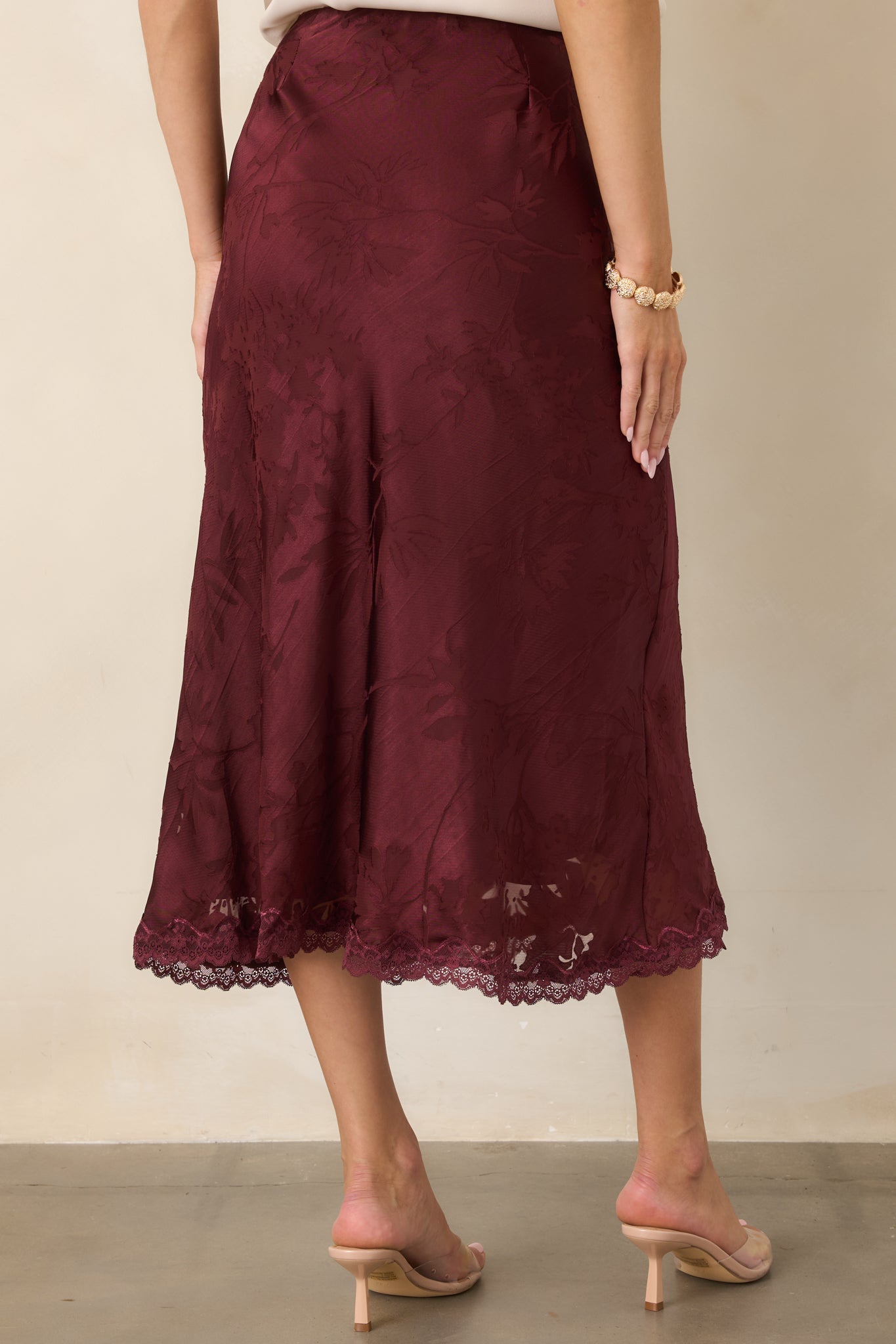 Rear view of the floral satin midi skirt showcasing its bias-cut drape, softly curved silhouette, lace-trimmed hem, and polished finish.