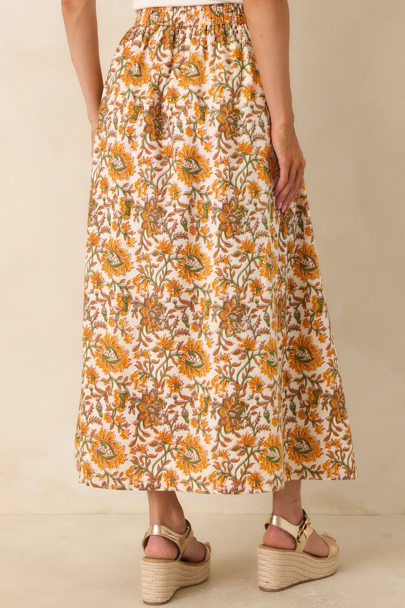 Rear view of the flowing maxi skirt featuring an elastic waistband and a marigold and olive floral print on an ivory background.