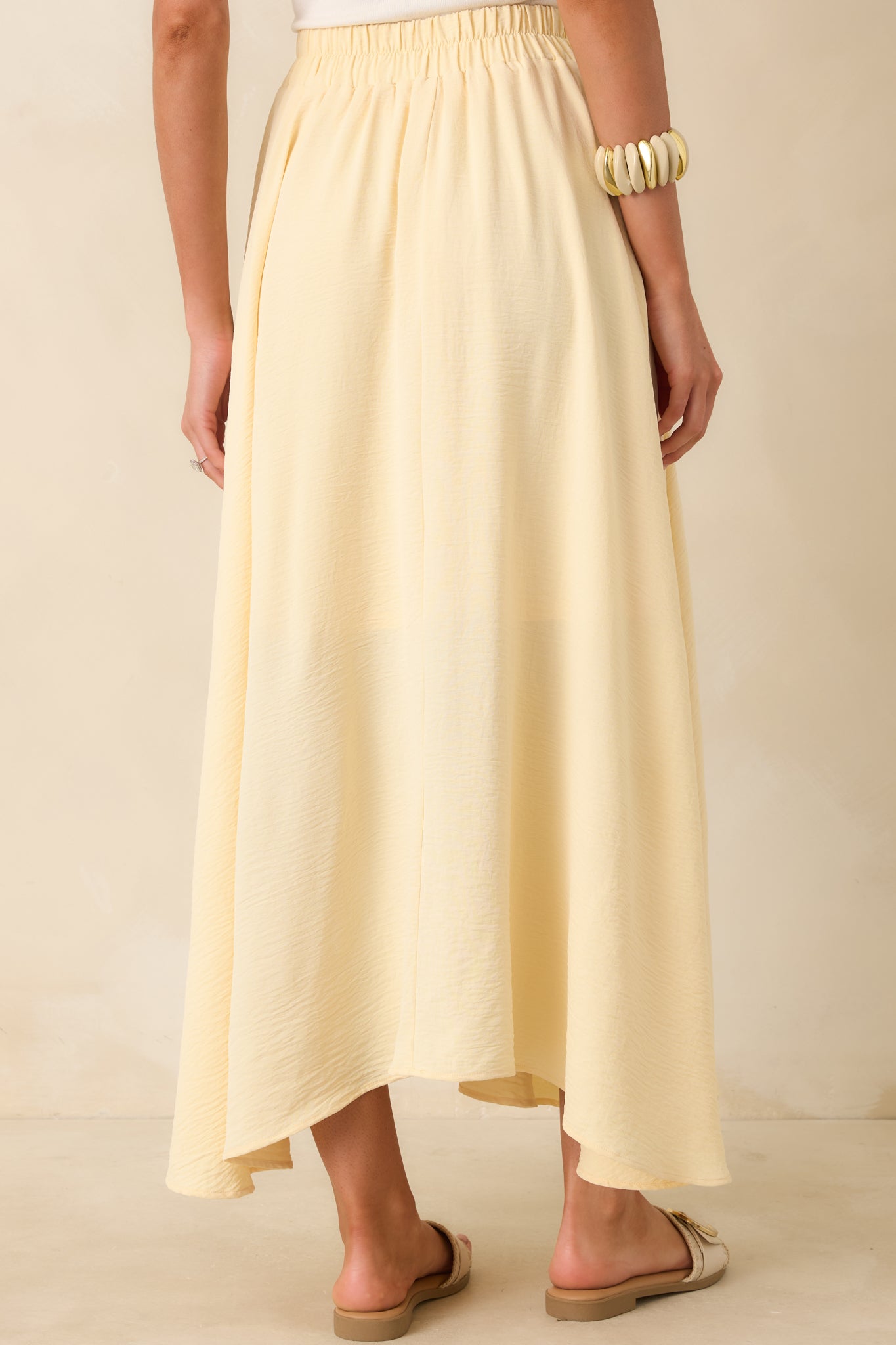 Rear view of the light yellow maxi skirt highlighting the flowy silhouette, curved hemline, and elastic waistband.
