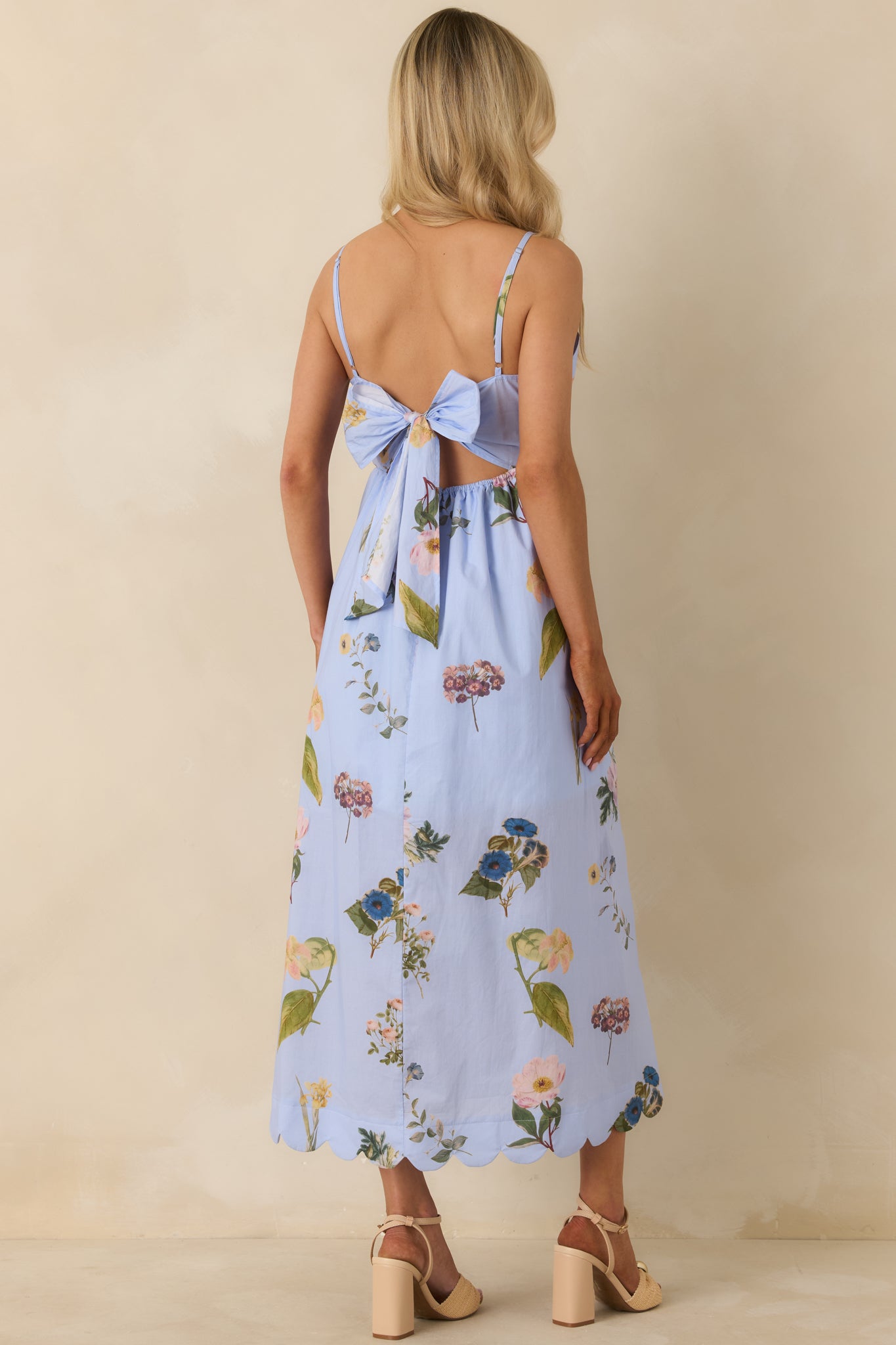 Rear view of blue midi dress highlighting tie-back detail, adjustable spaghetti straps, and scalloped hem with flowing skirt.