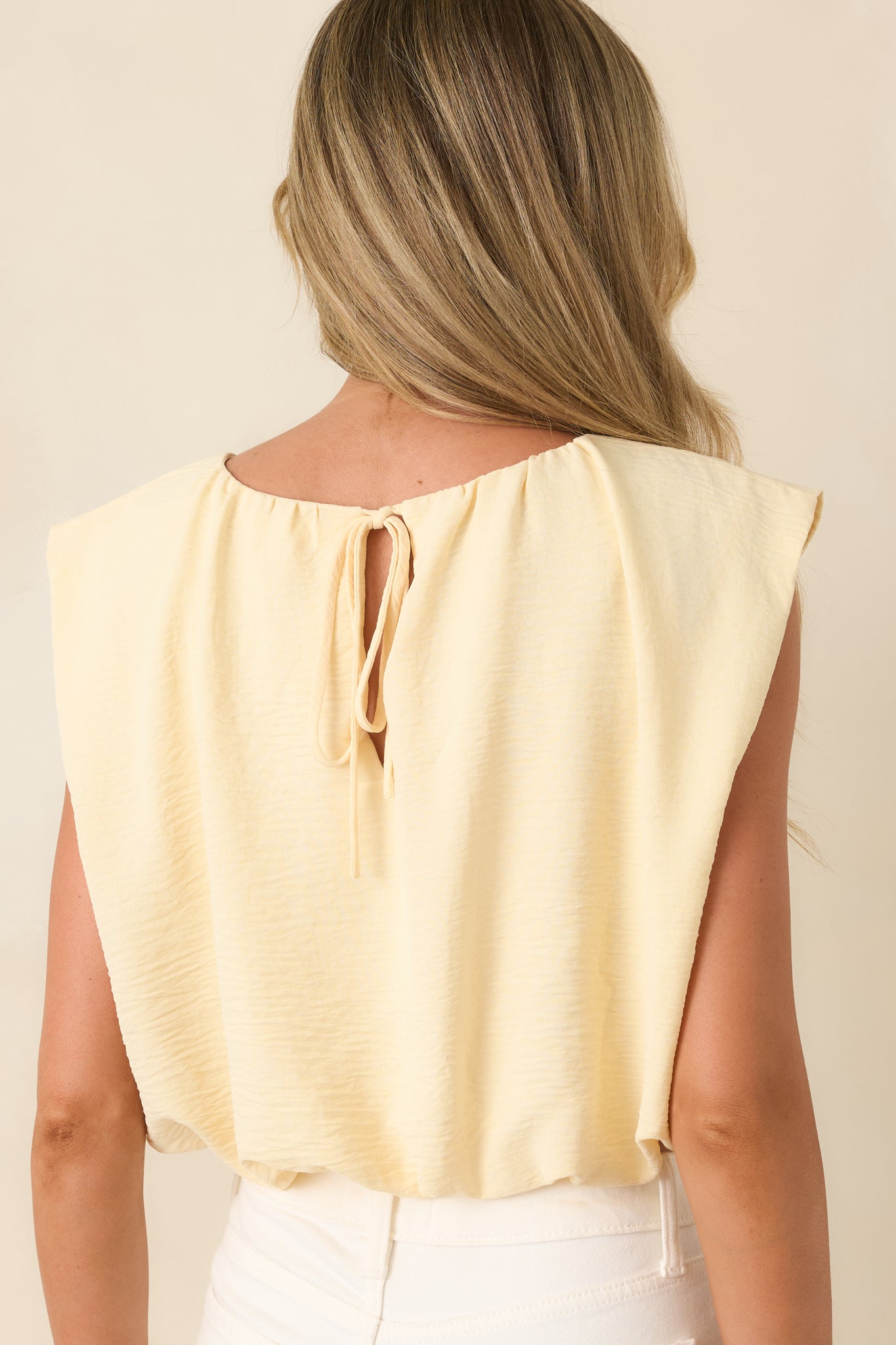 Rear view of the light yellow cropped top highlighting the tie-back keyhole closure and gathered sleeveless neckline.