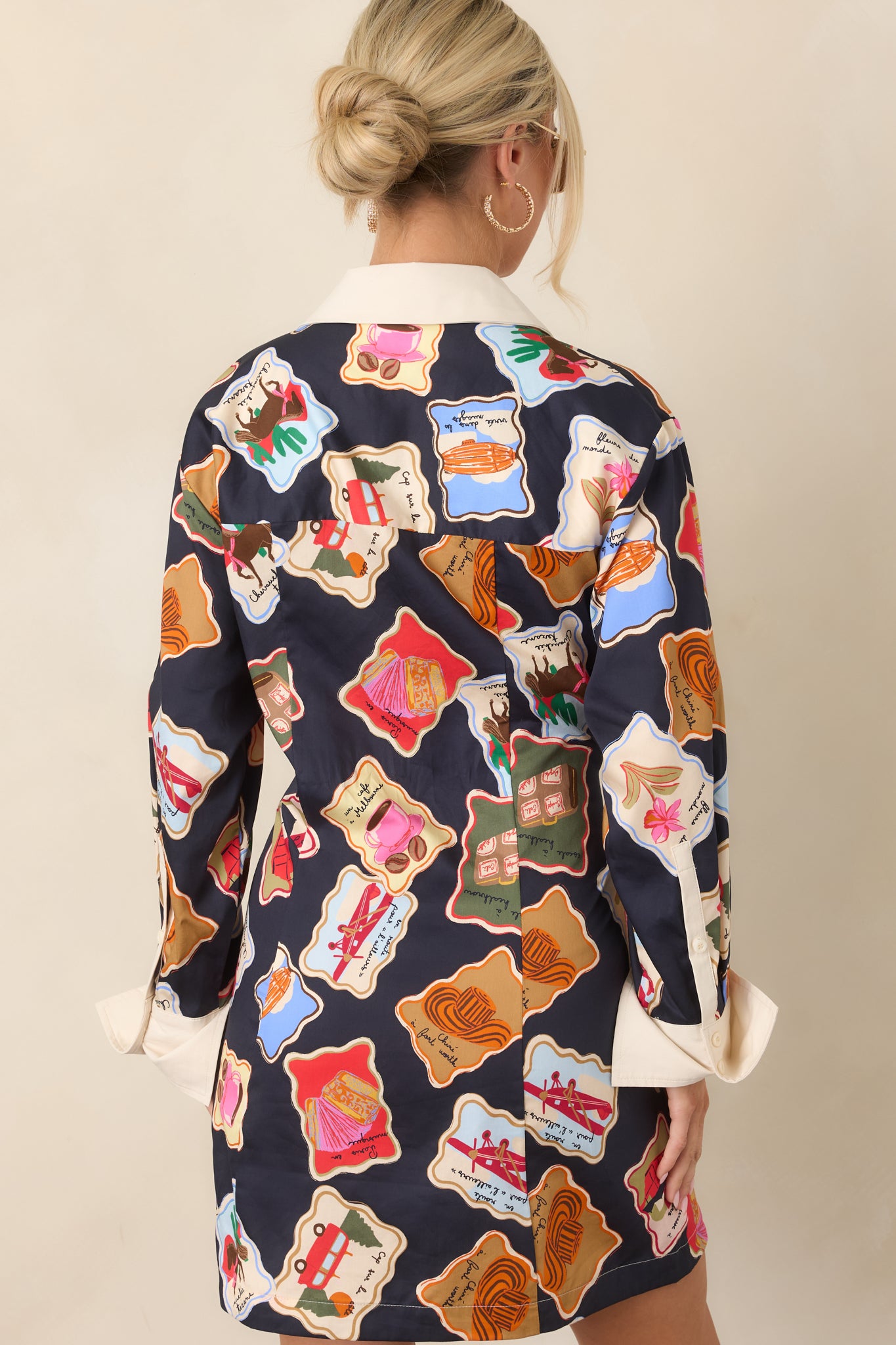 Rear view of the midnight blue mini dress displaying its scattered illustrated motifs, long sleeves, and polished mini-length silhouette.