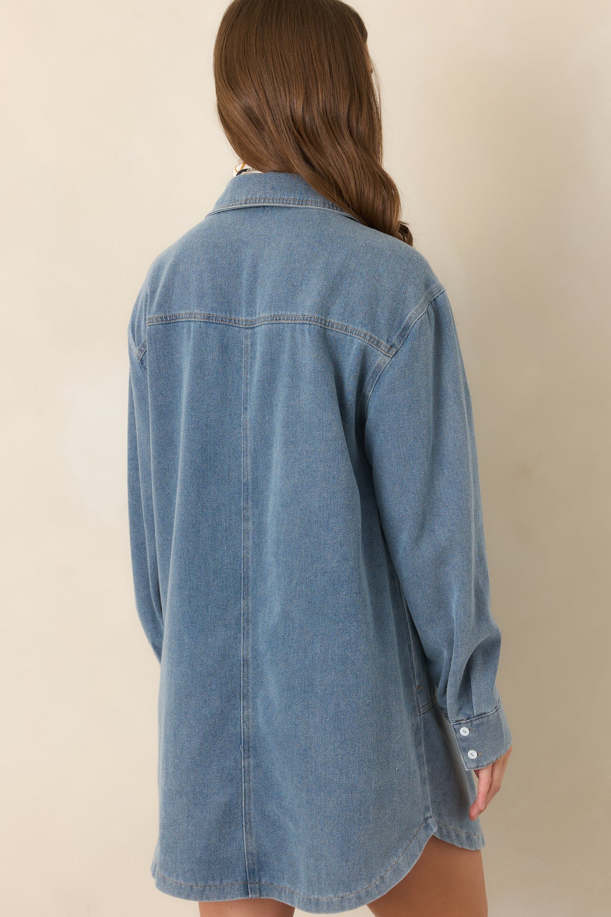 Rear view of the medium indigo denim mini dress showcasing its relaxed oversized silhouette, long cuffed sleeves, and straight hemline.