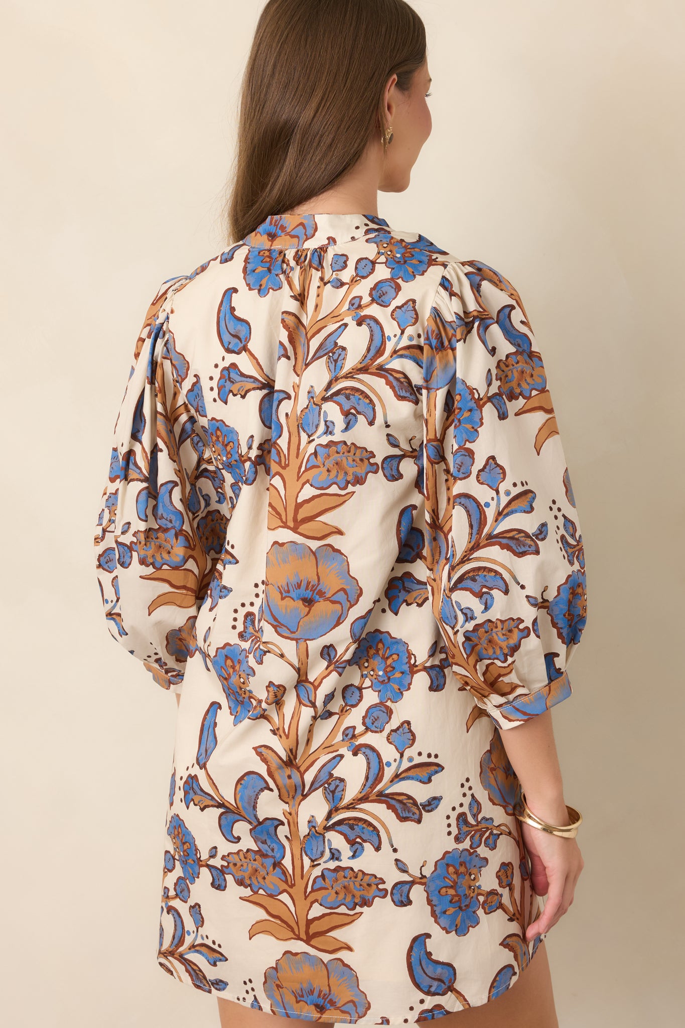 Rear view of the ivory cotton mini dress showcasing its relaxed shift silhouette, gathered three-quarter sleeves, and floral print.