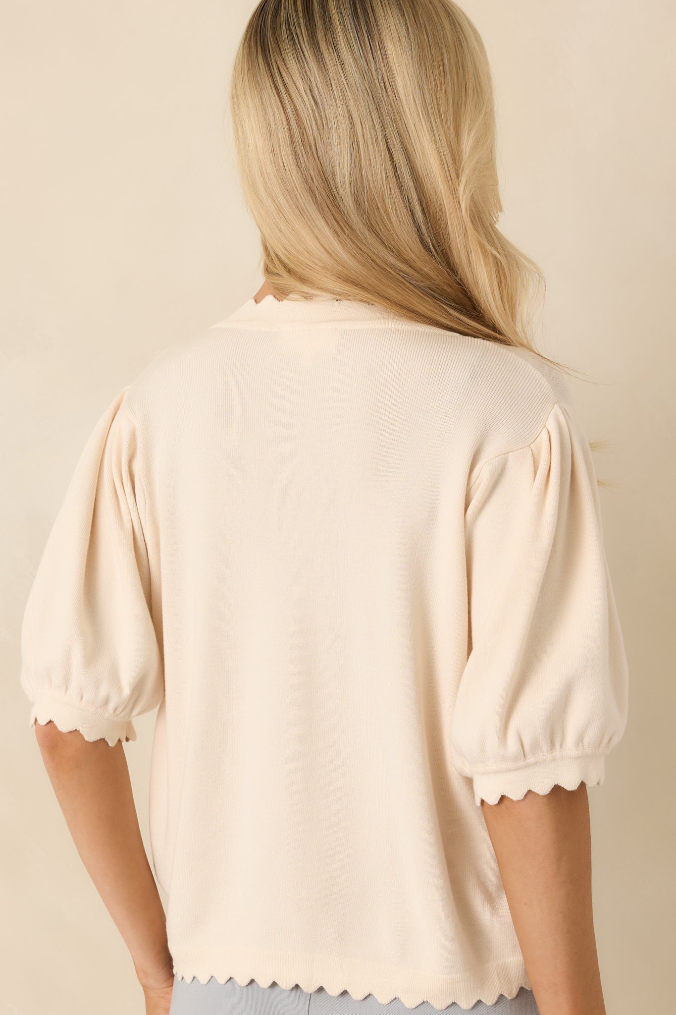 Rear photo of ivory knit cardigan featuring scalloped hem edging and a soft, lightweight knit construction.