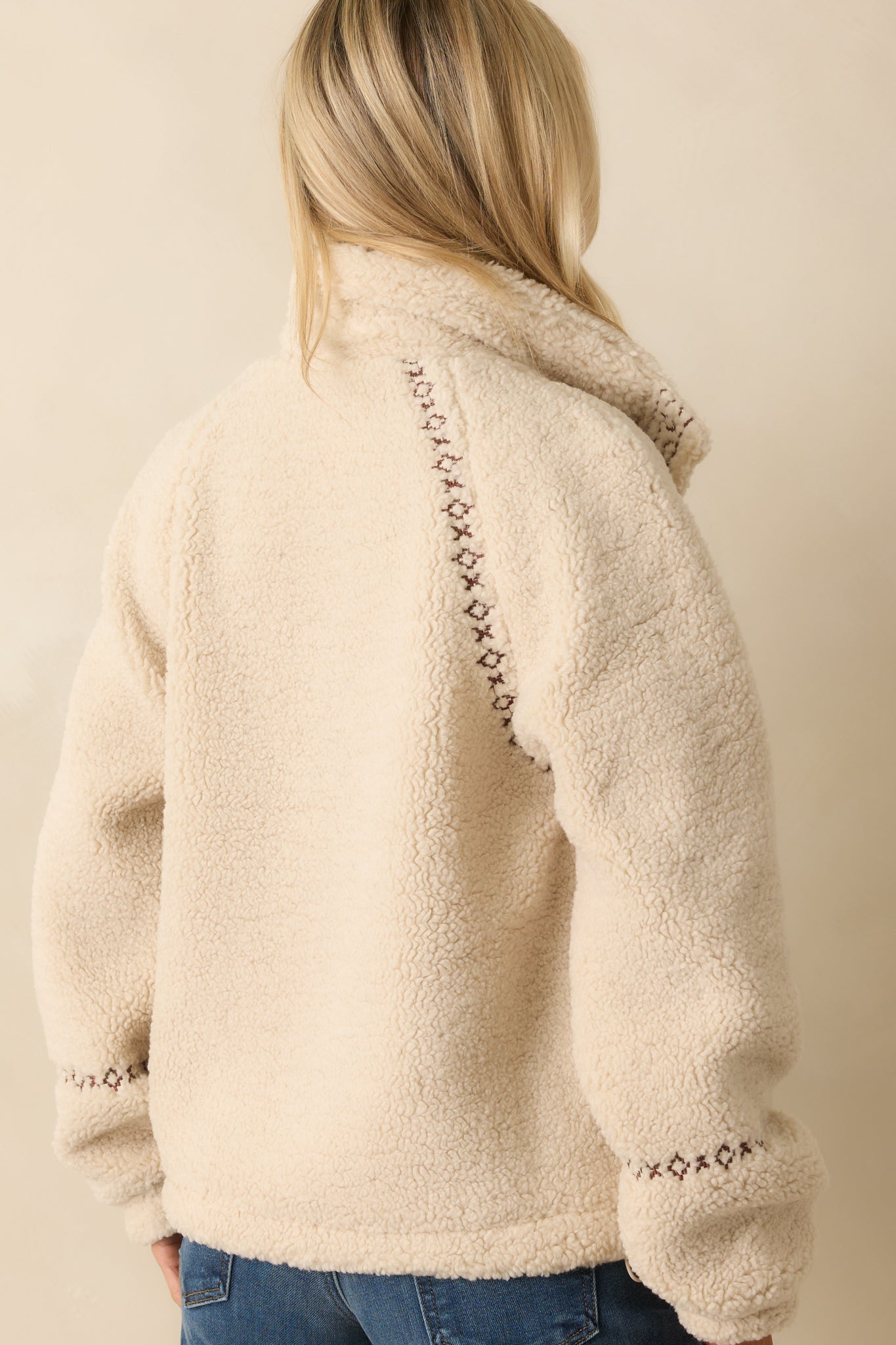 Rear view of ivory sherpa jacket with straight hemline, long sleeves, and subtle embroidered trim along the shoulders.