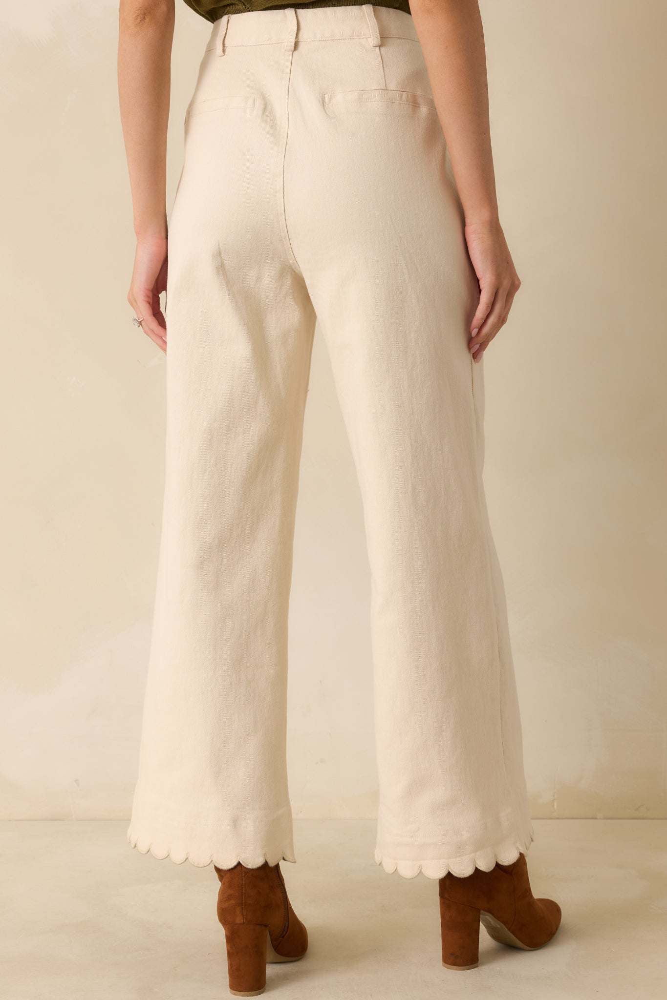 Rear view of ivory wide-leg pants showing back welt pockets, belt loops, and scalloped hemline.