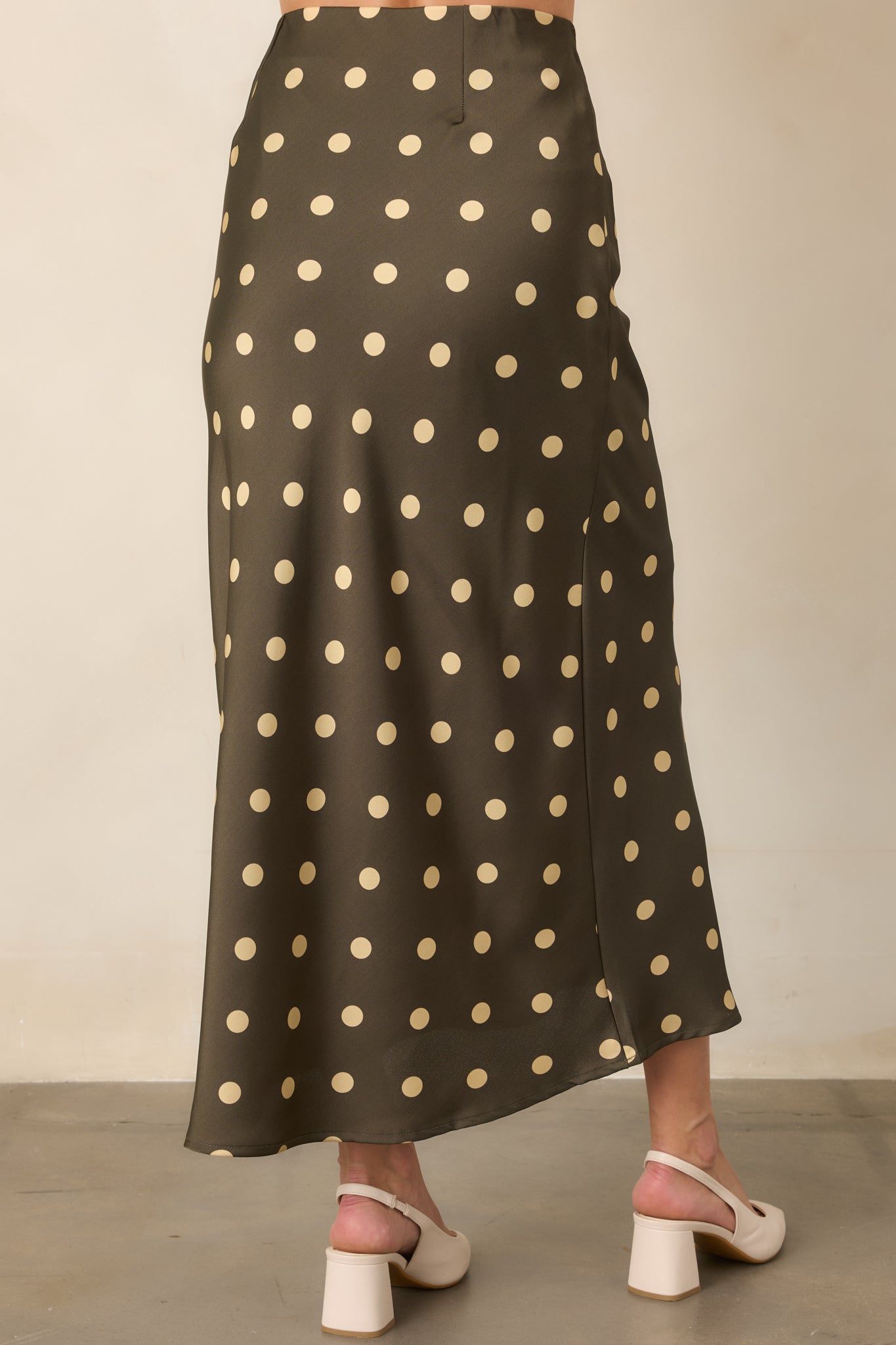 Rear view of the moss green satin skirt showcasing its fluid bias-cut silhouette, cream polka dot pattern, and elastic waistband.