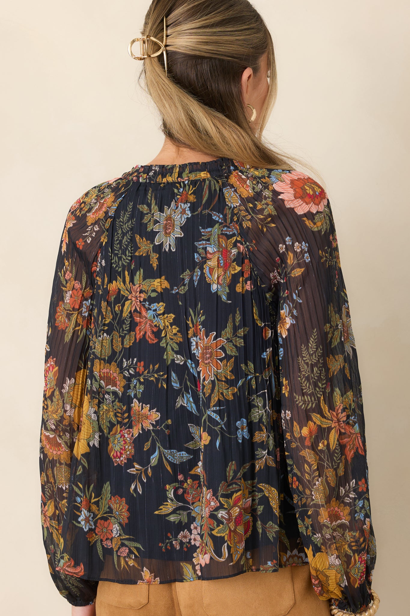 Rear view of the deep navy botanical top showcasing its pleated texture and long sheer balloon sleeves with elasticized cuffs.