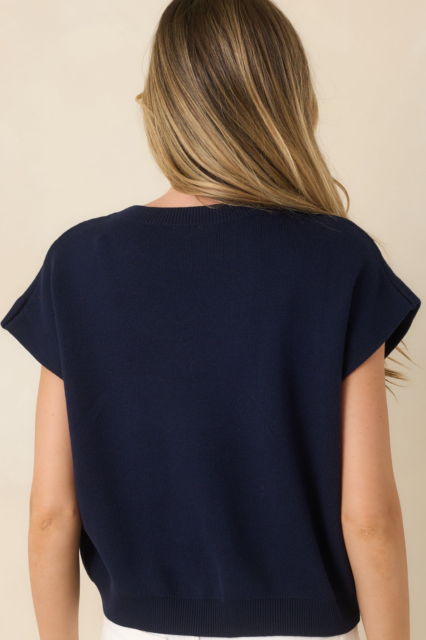 Rear view of the navy knit sweater featuring a relaxed silhouette, cap sleeves, ribbed neckline, and smooth knit finish.