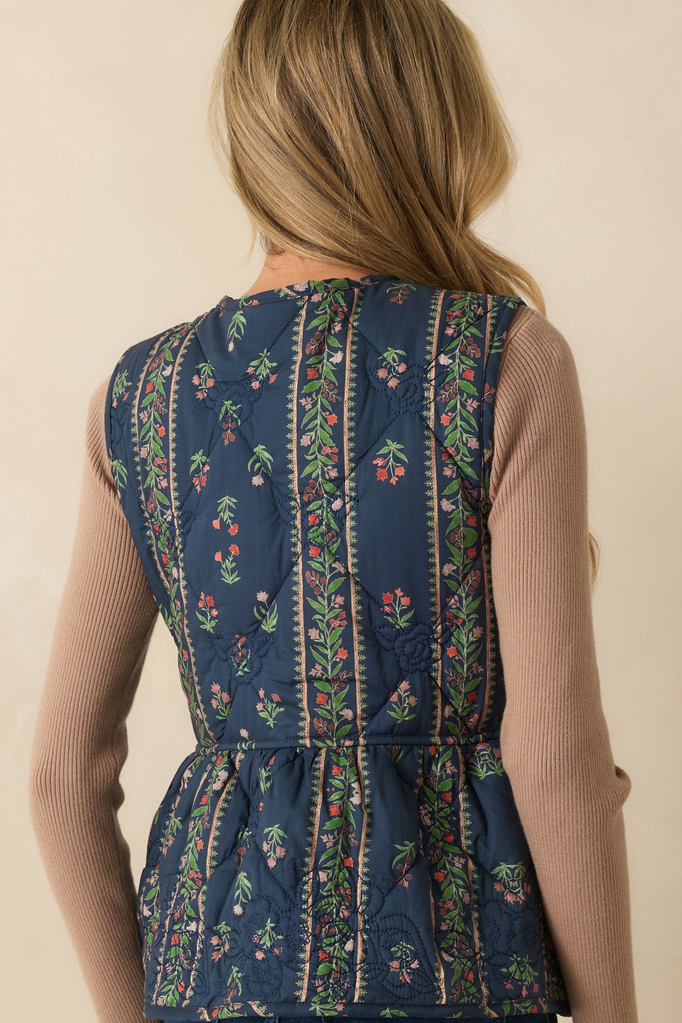 Rear view of the navy quilted vest showing peplum silhouette and floral embroidery