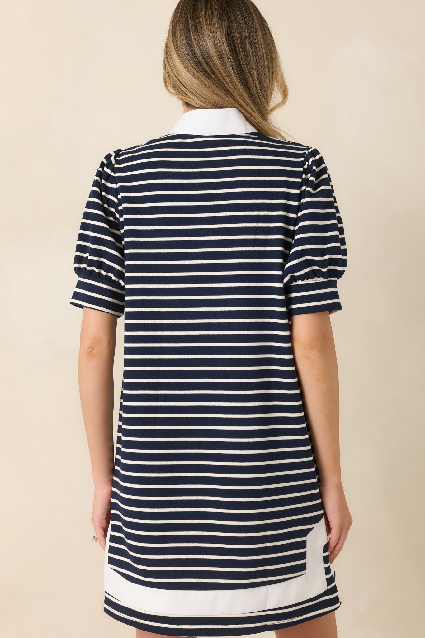 Rear view of the navy and white striped mini dress featuring a relaxed shift silhouette, puff sleeves, and white contrast trim at the hem.