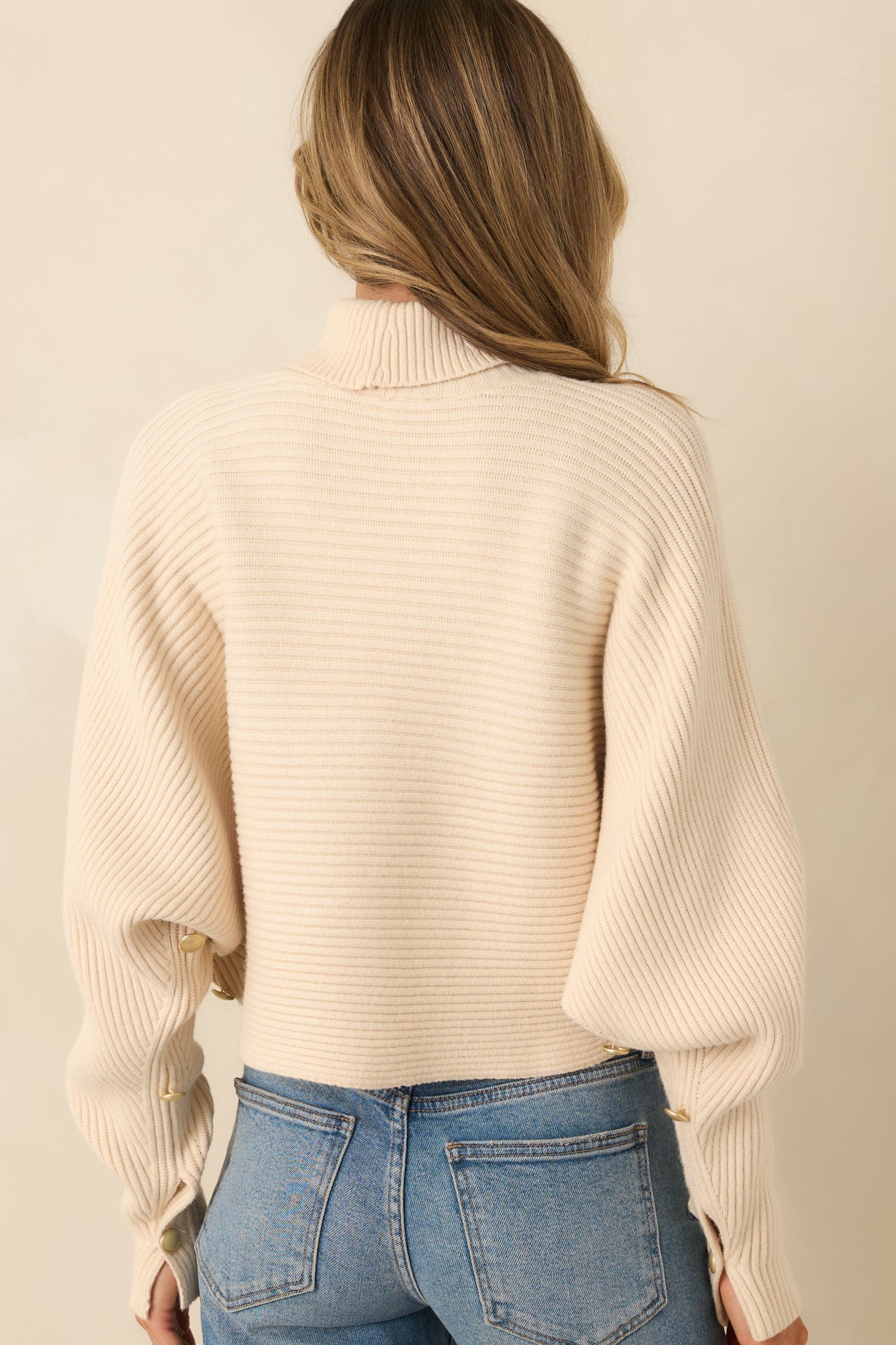 Rear view of beige sweater showing relaxed batwing sleeves and cropped hem.