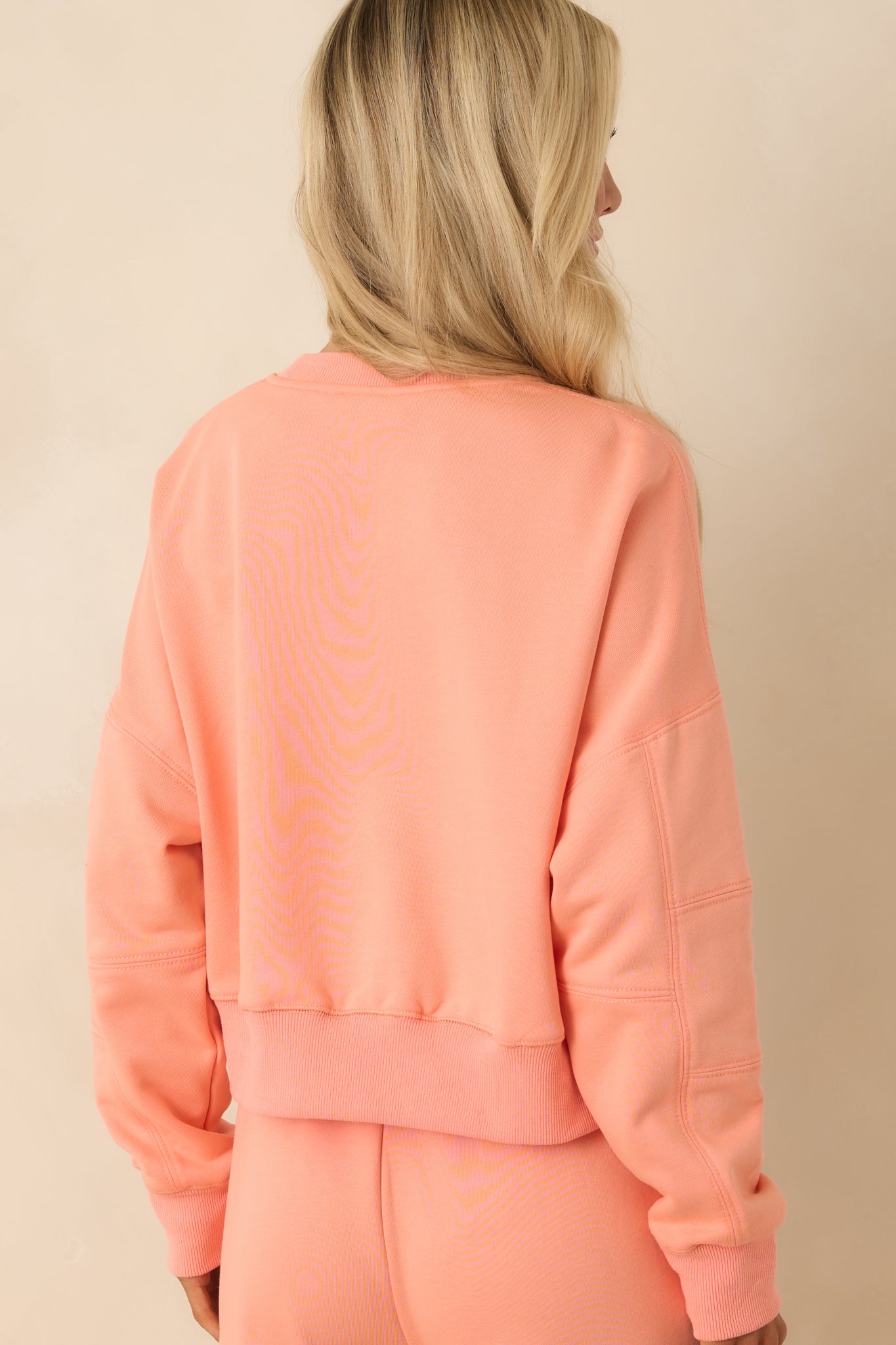 Rear view of coral orange sweatshirt showing relaxed fit and ribbed hem and cuffs.