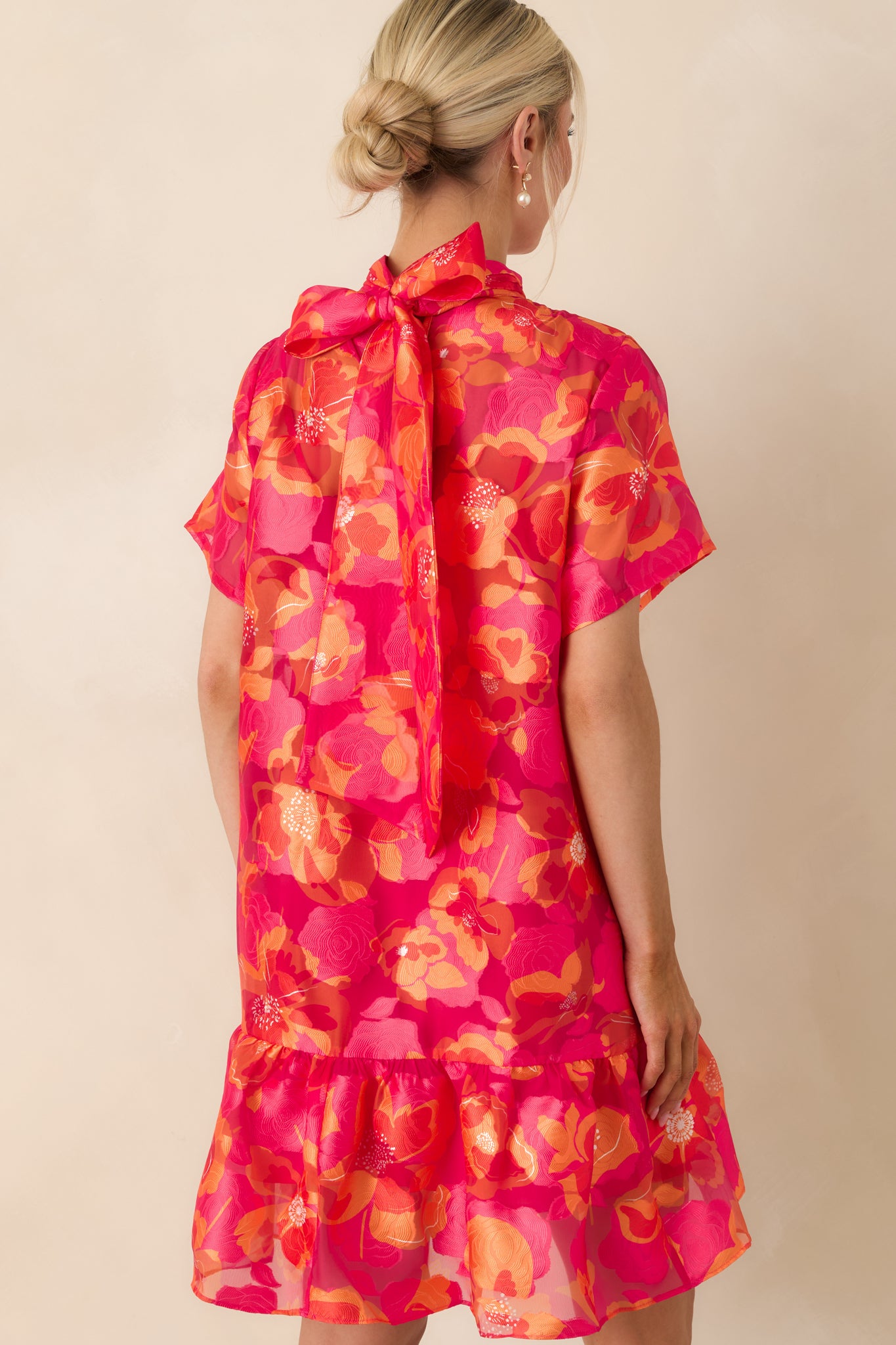 Rear view of mini dress with self-tie bow at back neckline, short sleeves, and flowing tiered hem.