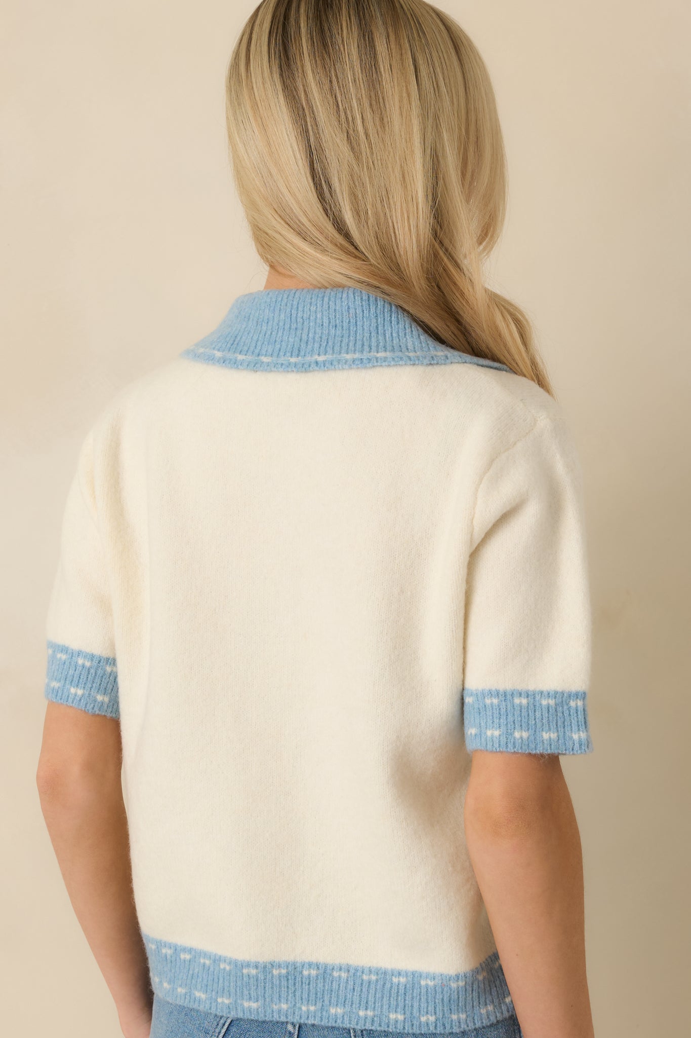 Rear view of ivory cardigan featuring light blue trim at the collar and hem with a smooth, structured finish.