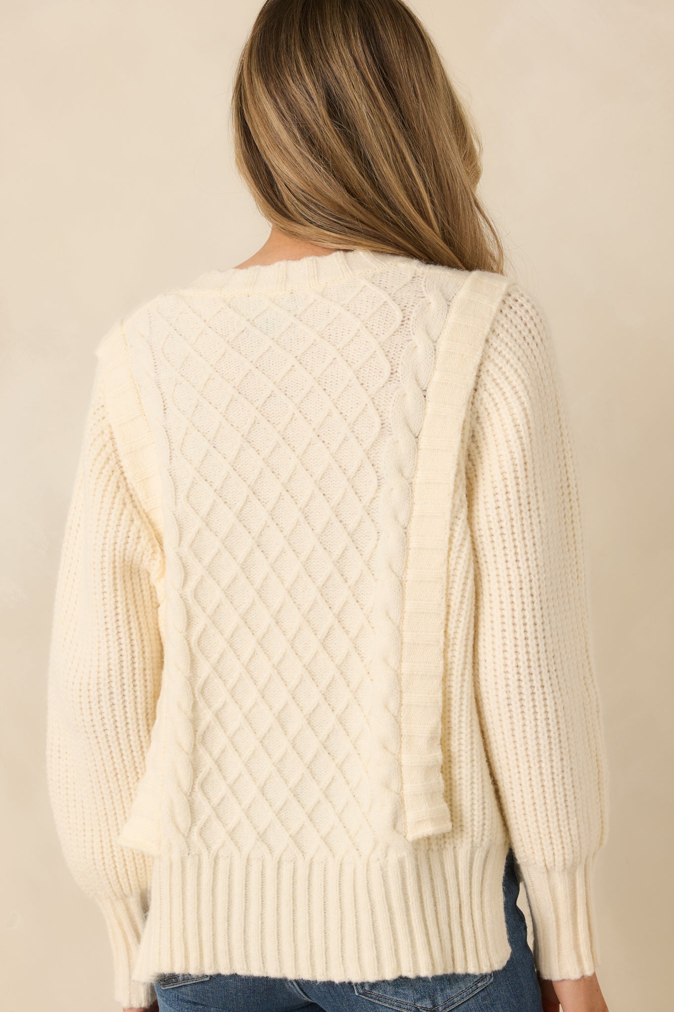 Rear view of ivory V-neck knit sweater with continuous textured panel detailing and ribbed trim.