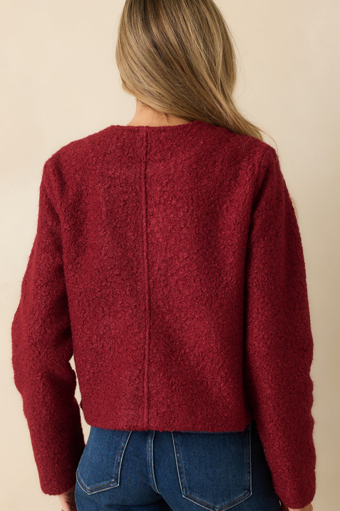 Rear view of the cherry red bouclé jacket highlighting the long sleeves and structured silhouette.
