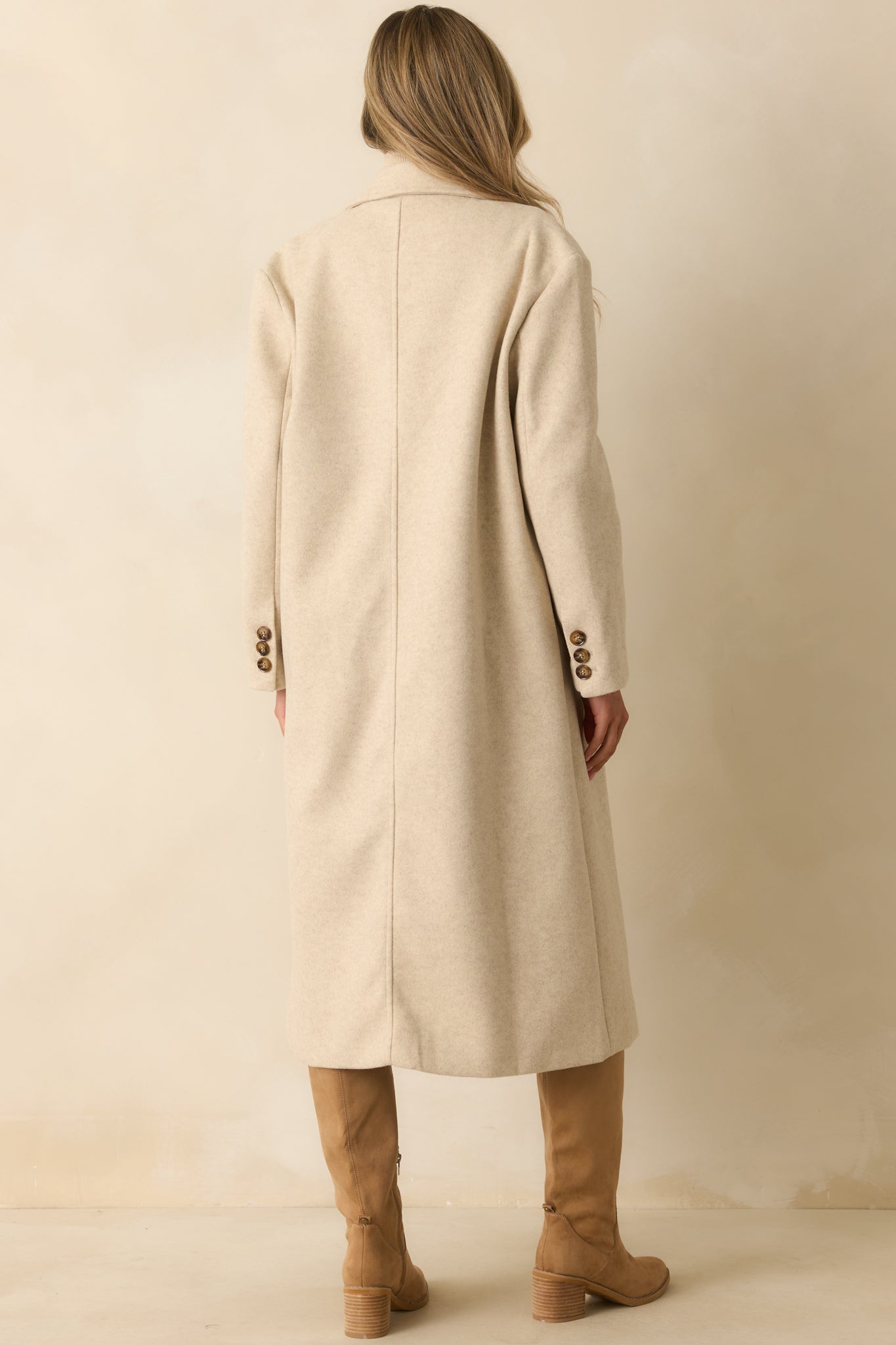 Rear view of the light beige longline coat with back vent and long sleeves.
