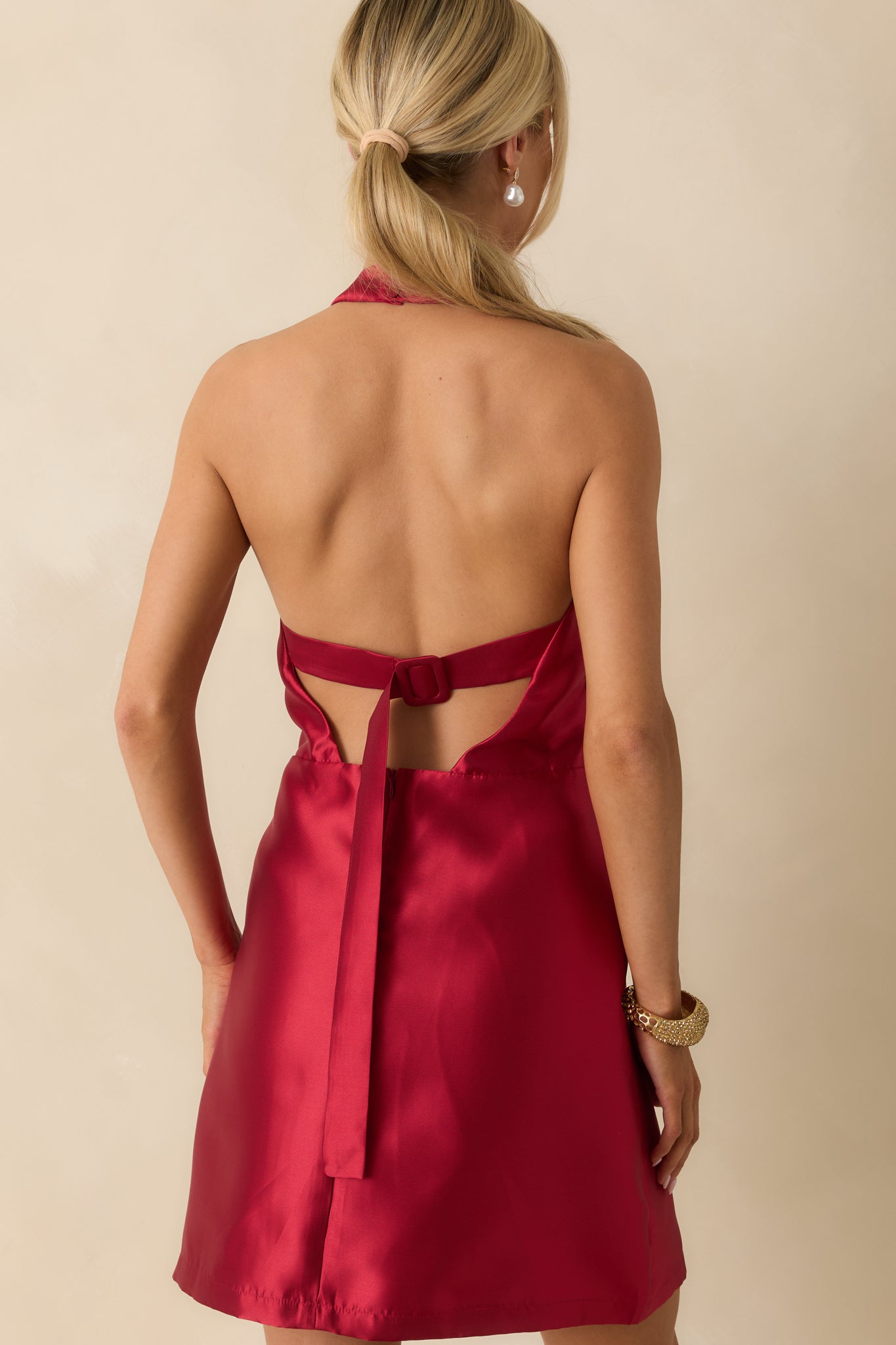 Rear view of red satin mini dress featuring open back with buckle strap and back zipper closure.