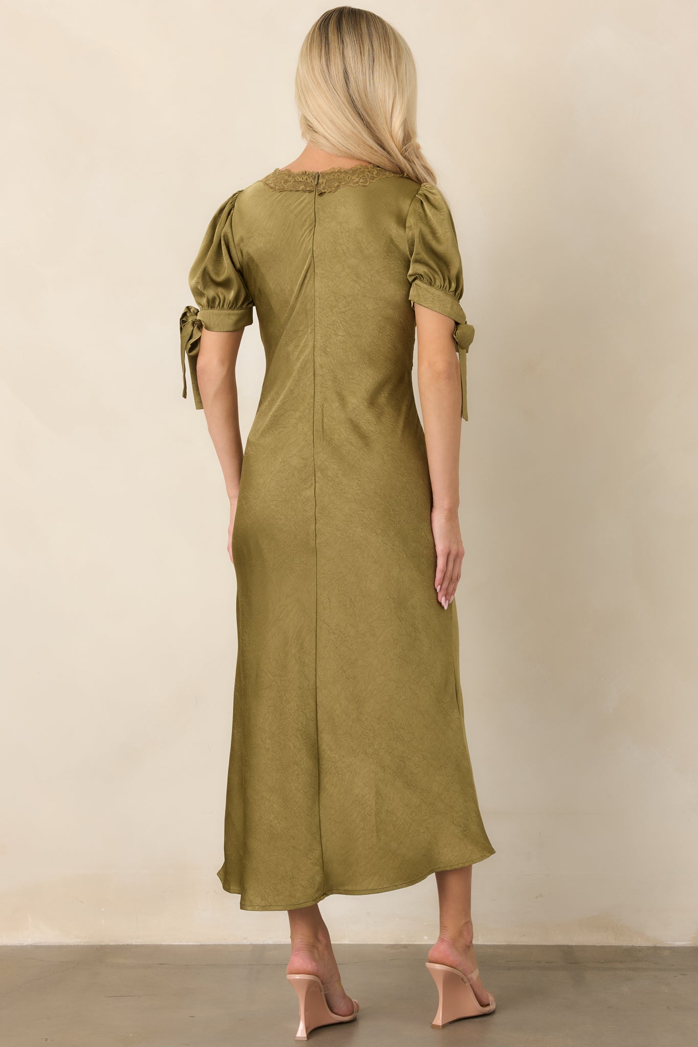Rear view of the olive green satin midi dress showing the smooth lined finish, puff sleeves, flowing skirt, and concealed back zipper.