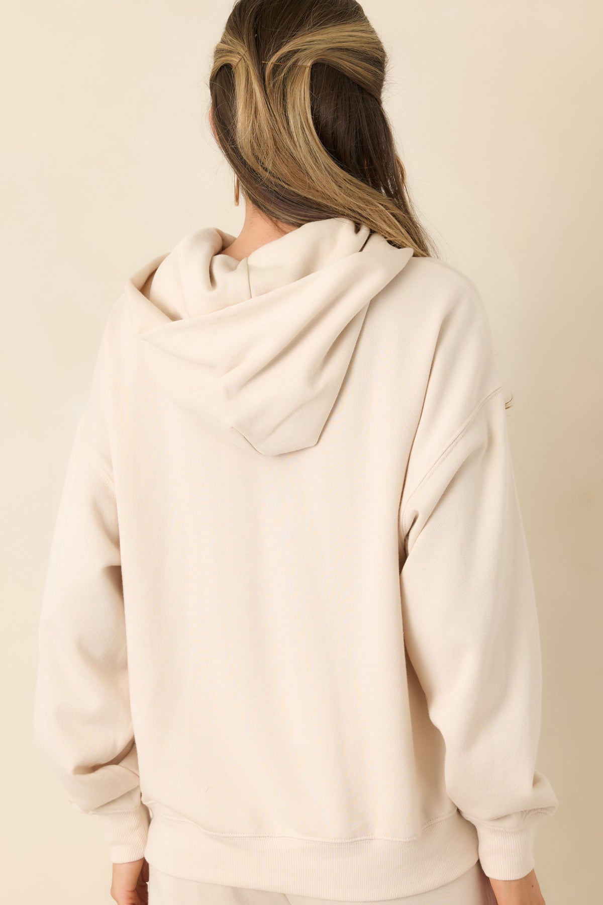 Rear view of the oversized cream hoodie with a roomy hood and relaxed sleeves.