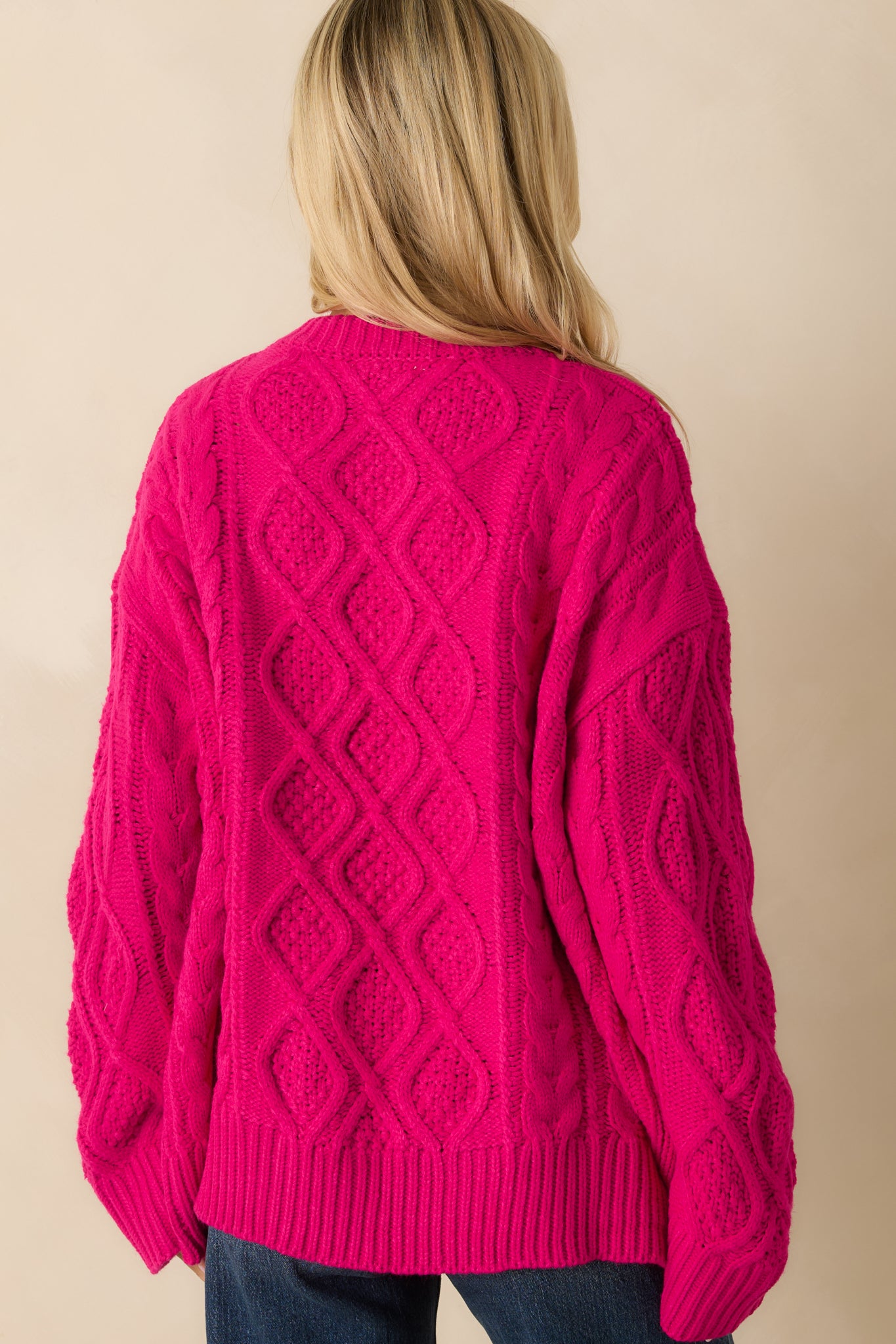 Rear view of the hot pink cable knit sweater showing the oversized fit and ribbed hem.