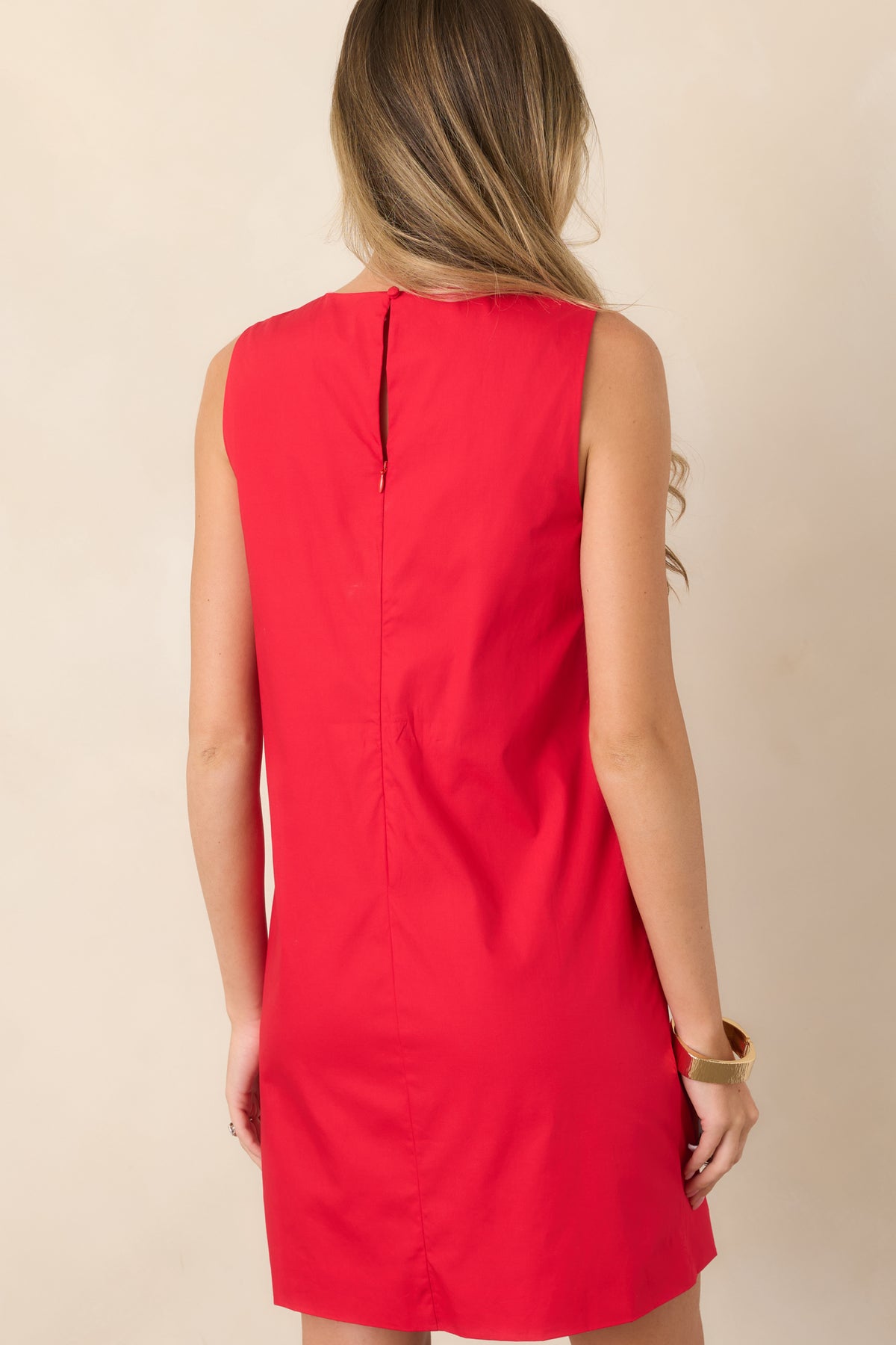 Rear view of the structured pink sleeveless mini dress showcasing its clean silhouette and red contrast trim framing the edges.