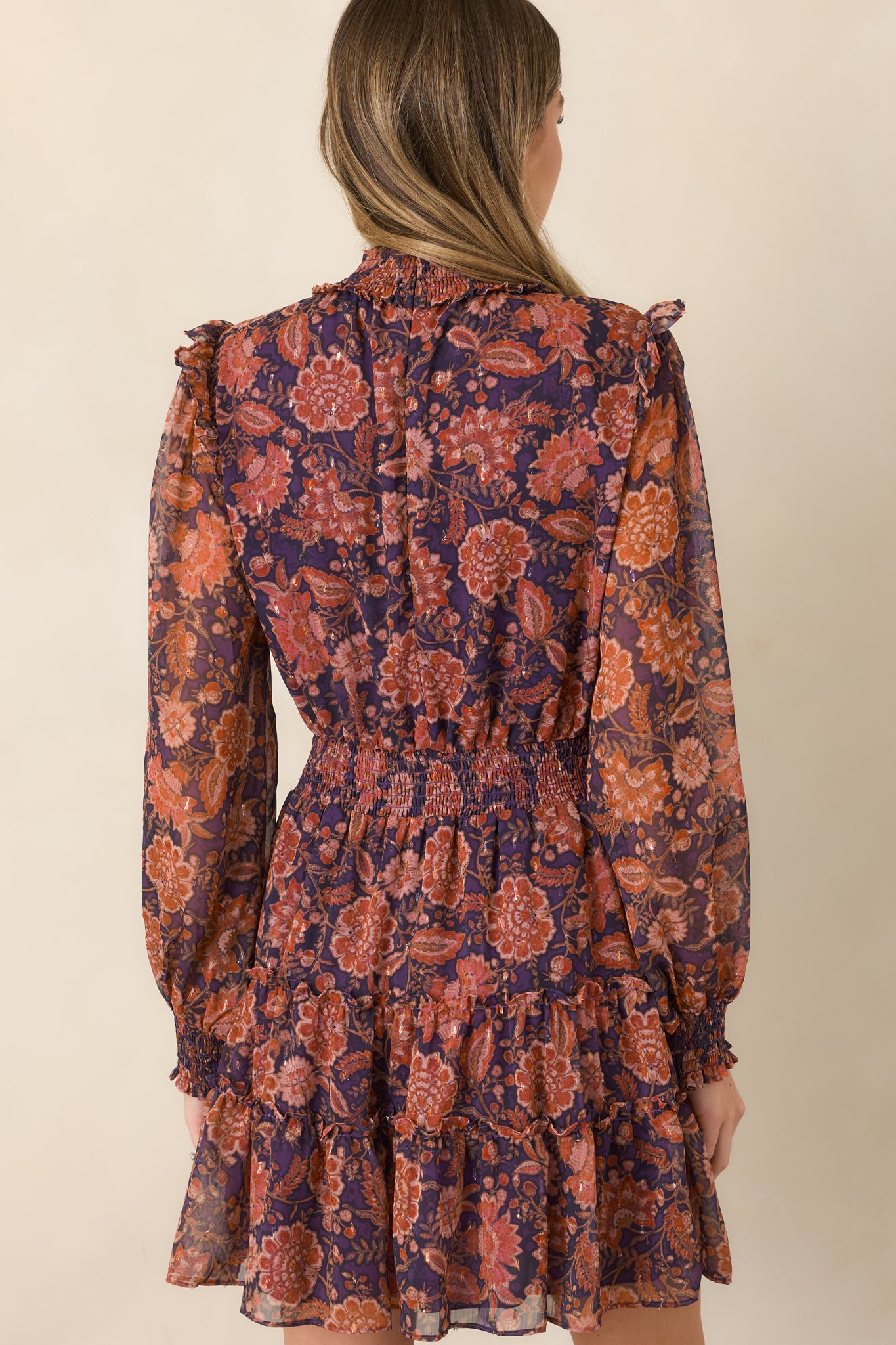 Rear view of the deep plum floral mini dress featuring a wide smocked waist, sheer sleeves, and tiered skirt.