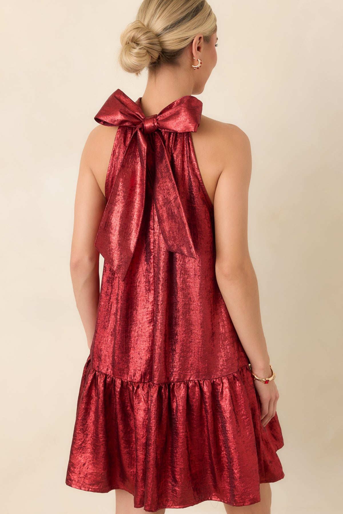 Rear of the lustrous red mini dress showcasing the large halter tie bow with long ends above the flared ruffle skirt.