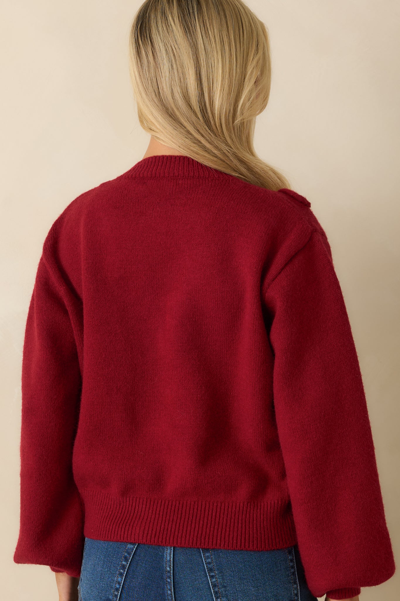 Rear view of red knit cardigan displaying long sleeves, round neckline, and clean knit back without embellishments.