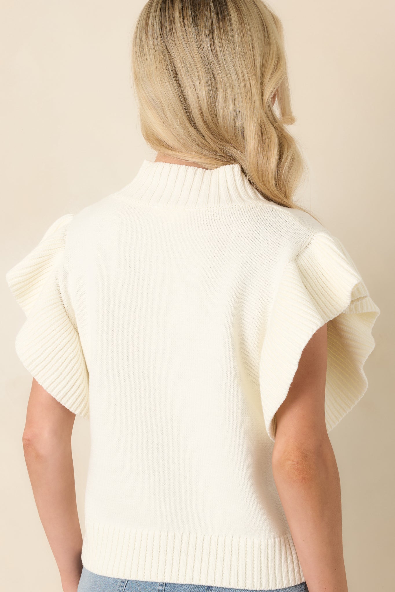 Rear view of the ivory knit top showcasing the relaxed fit, ribbed hem, and flutter sleeve design from behind.
