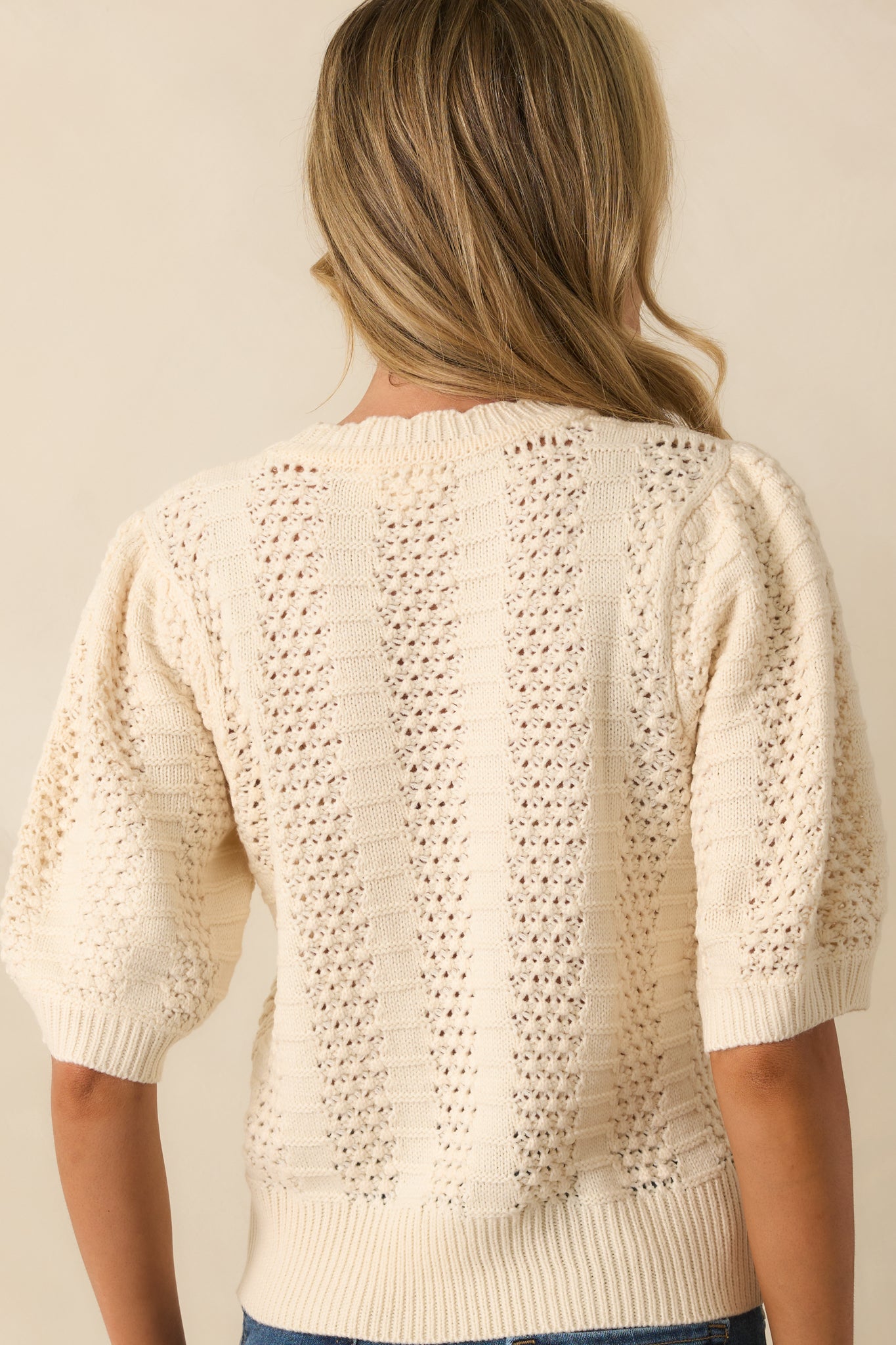 Rear view of the ivory sweater showing short sleeves and alternating vertical knit panels.