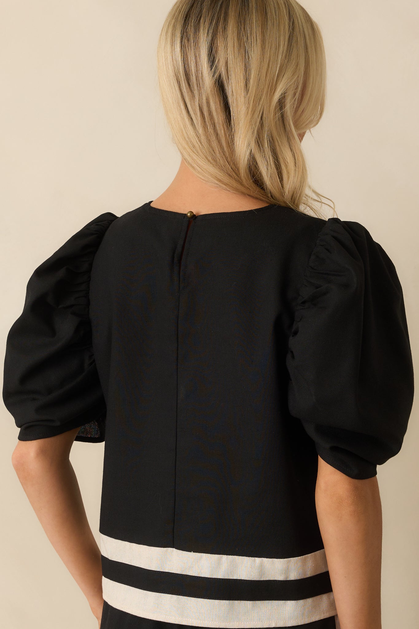 Rear view showing the black top’s keyhole button closure and ivory-trimmed neckline.