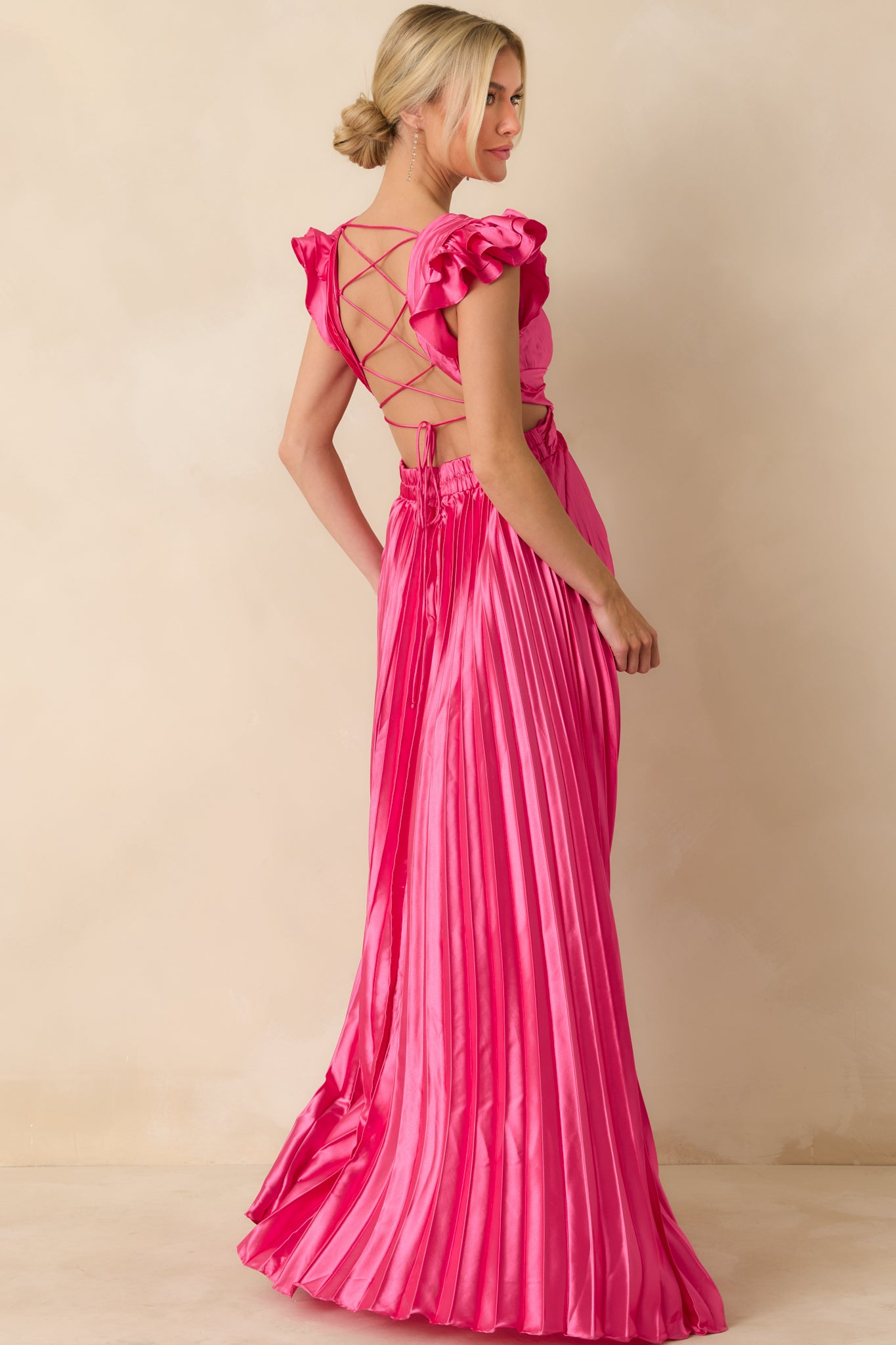Rear view of hot pink pleated maxi dress showing lace-up open back, elasticized waistband, and full pleated skirt.