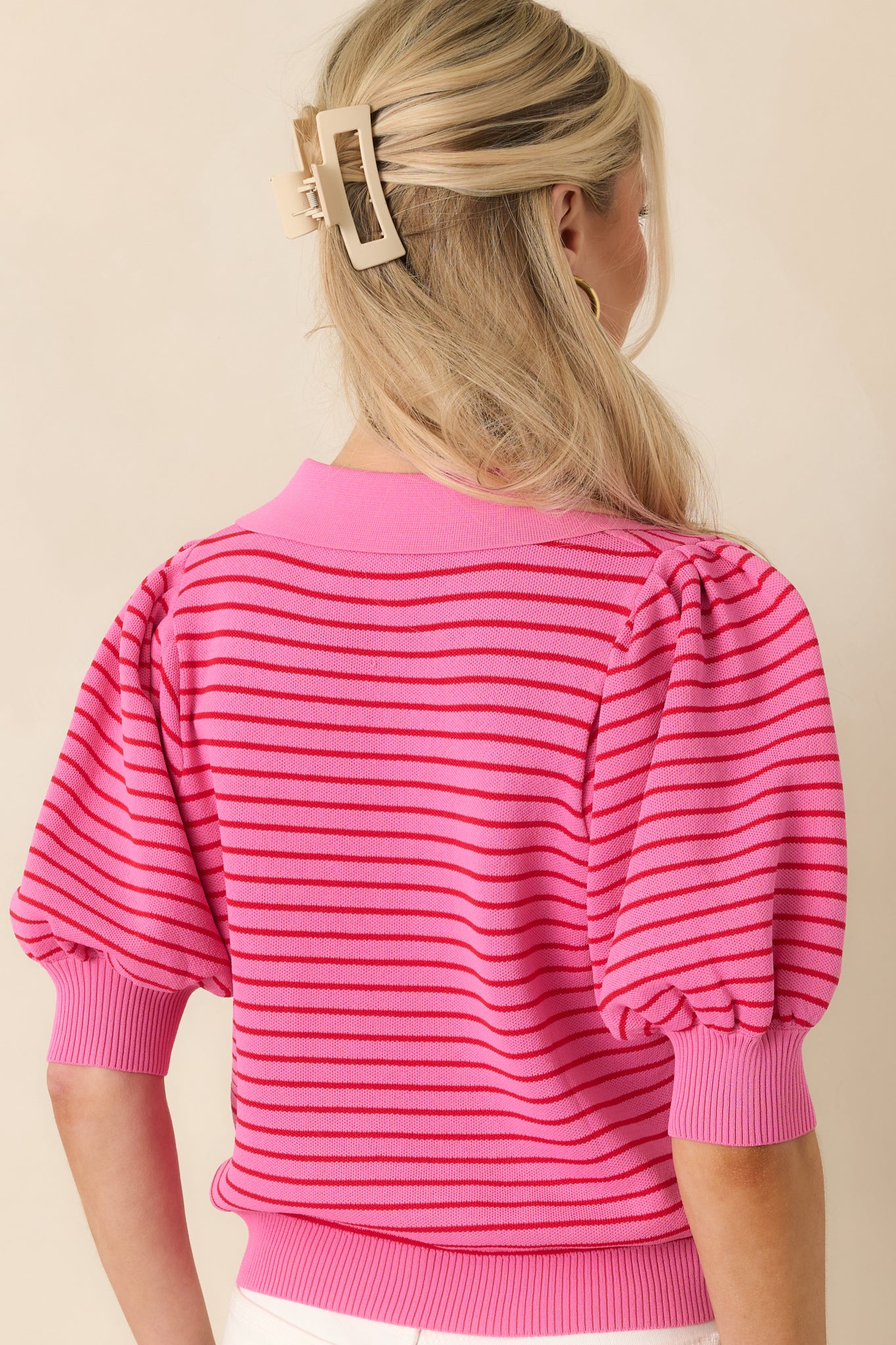 Rear view of the pink striped knit polo showing the puff sleeves, ribbed hem, and smooth knit fabric.
