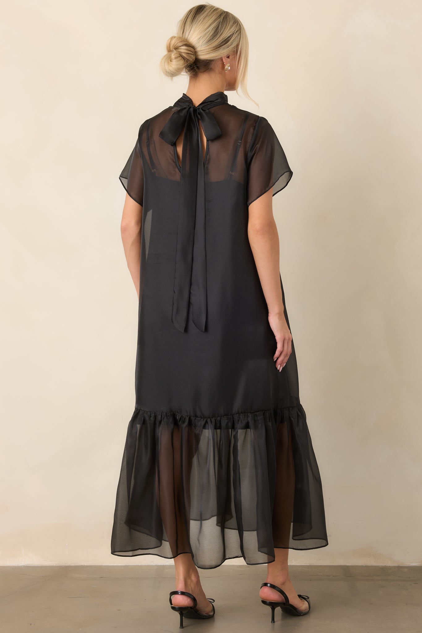 Rear view of the flowing organza maxi dress highlighting the tie-back neckline, sheer overlay, and gathered ruffle detailing at the hem.
