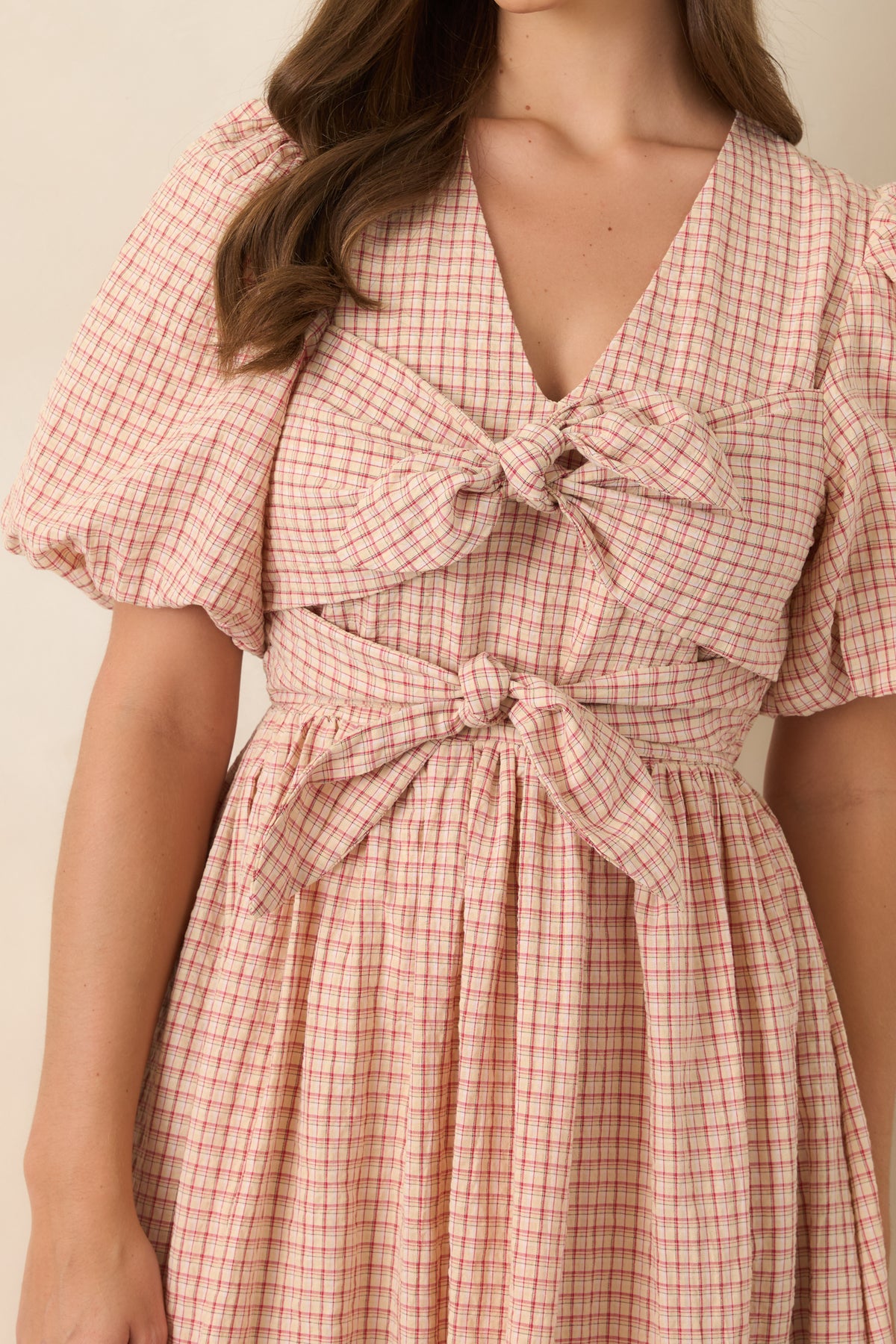 Close-up of the red and beige plaid dress highlighting the oversized double front ties, fitted bodice, and detailed plaid pattern.